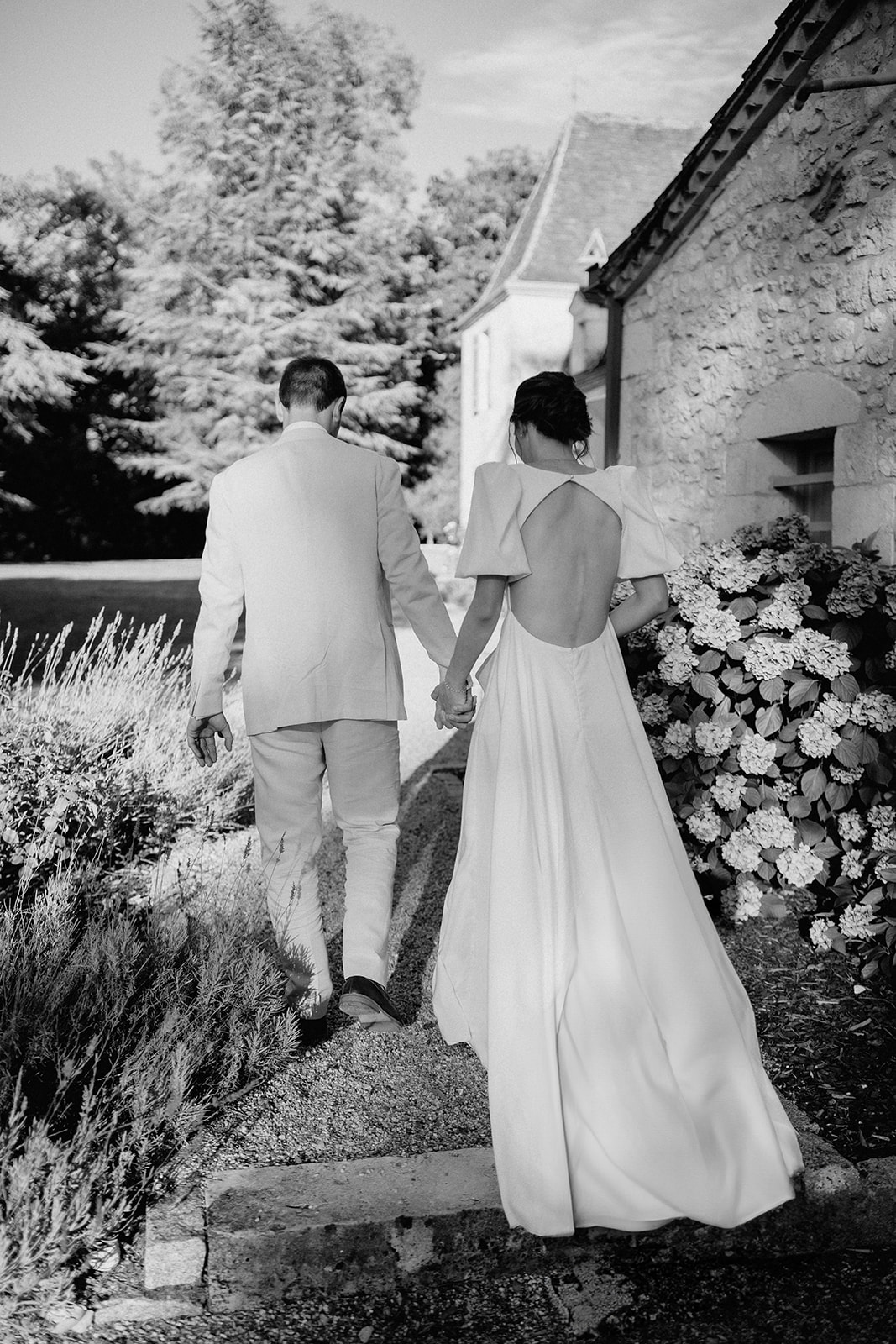 Bride and groom walking hand-in-hand along stone pathway at historic cottage garden venue