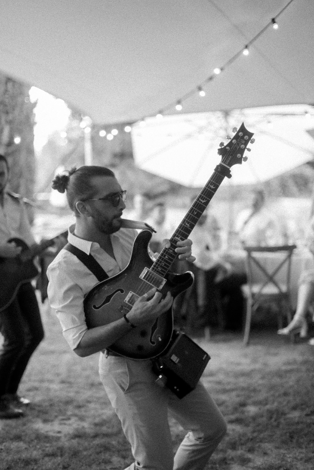 Musician performing electric guitar at outdoor wedding reception under marquee tent