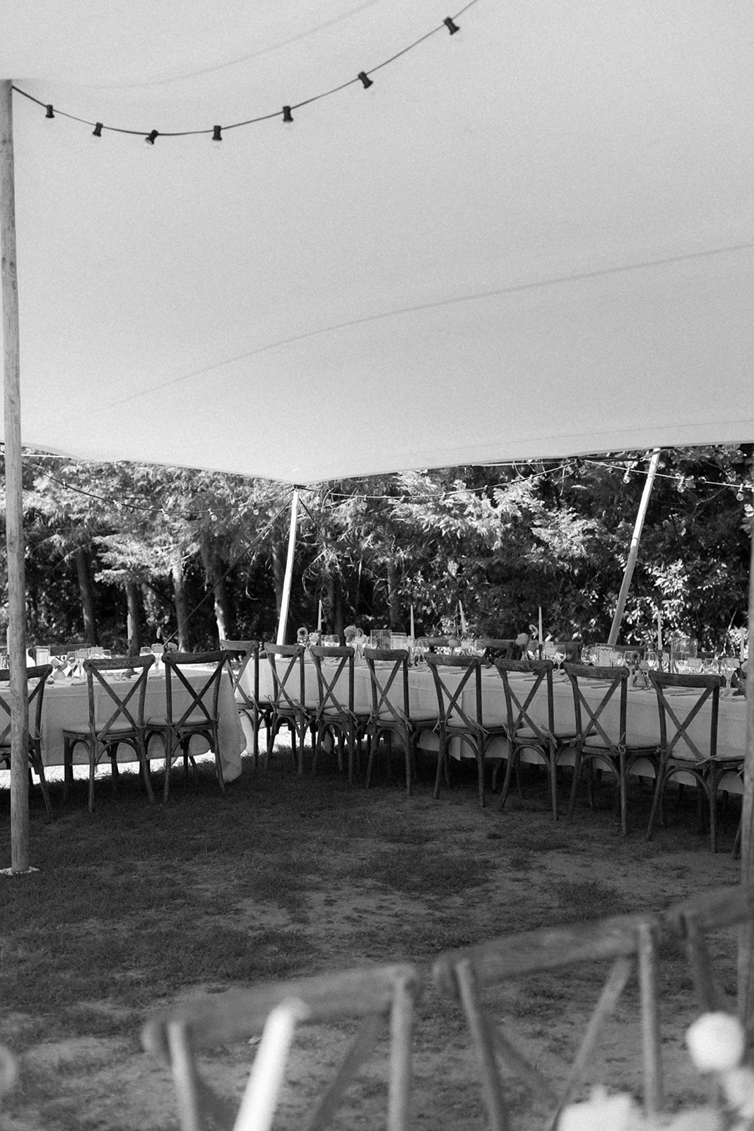 Outdoor reception setup with dining tables under canvas tent in wooded setting