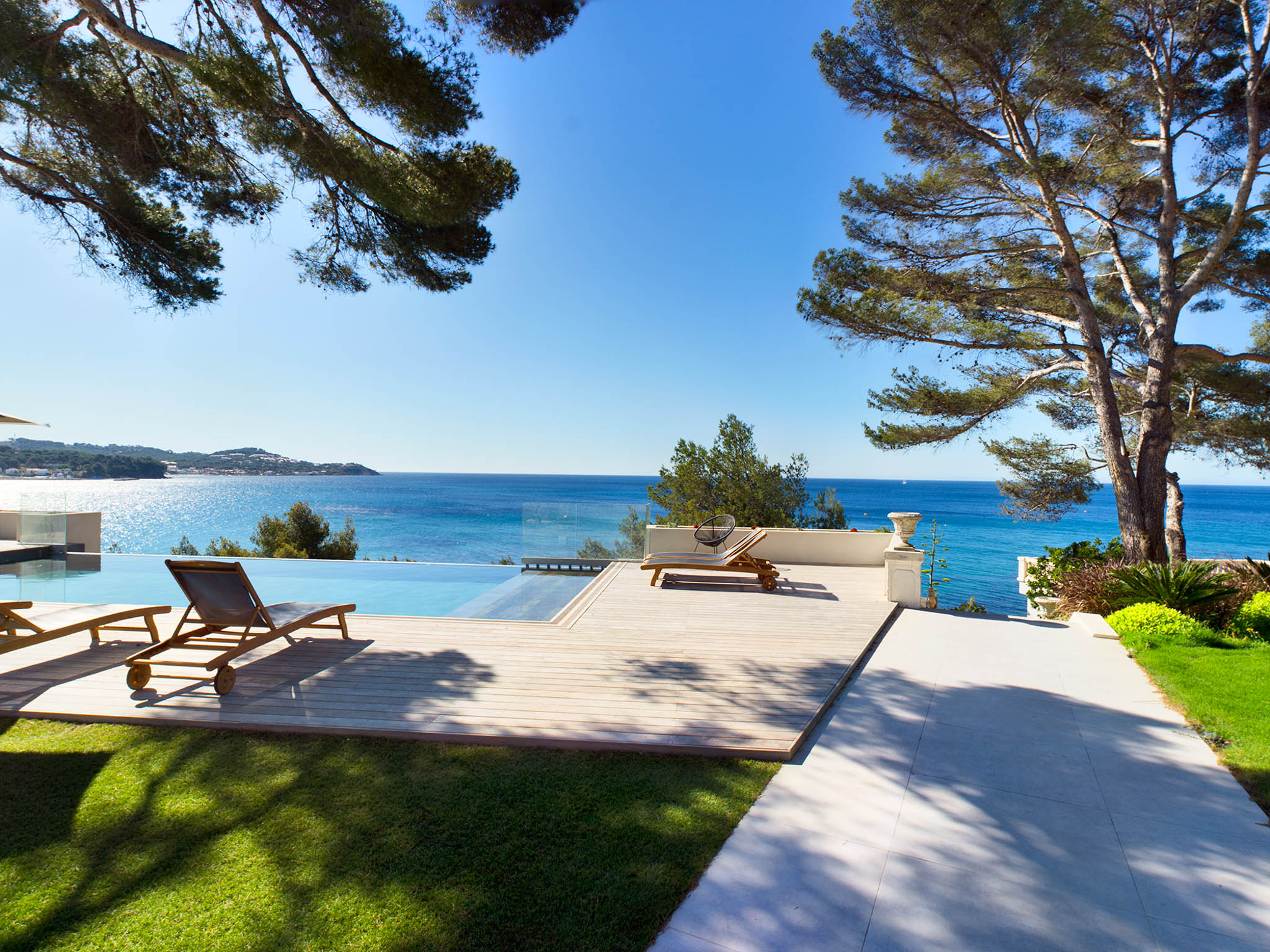 Timber deck terrace with infinity pool overlooking the sea, framed by pine trees and manicured lawn