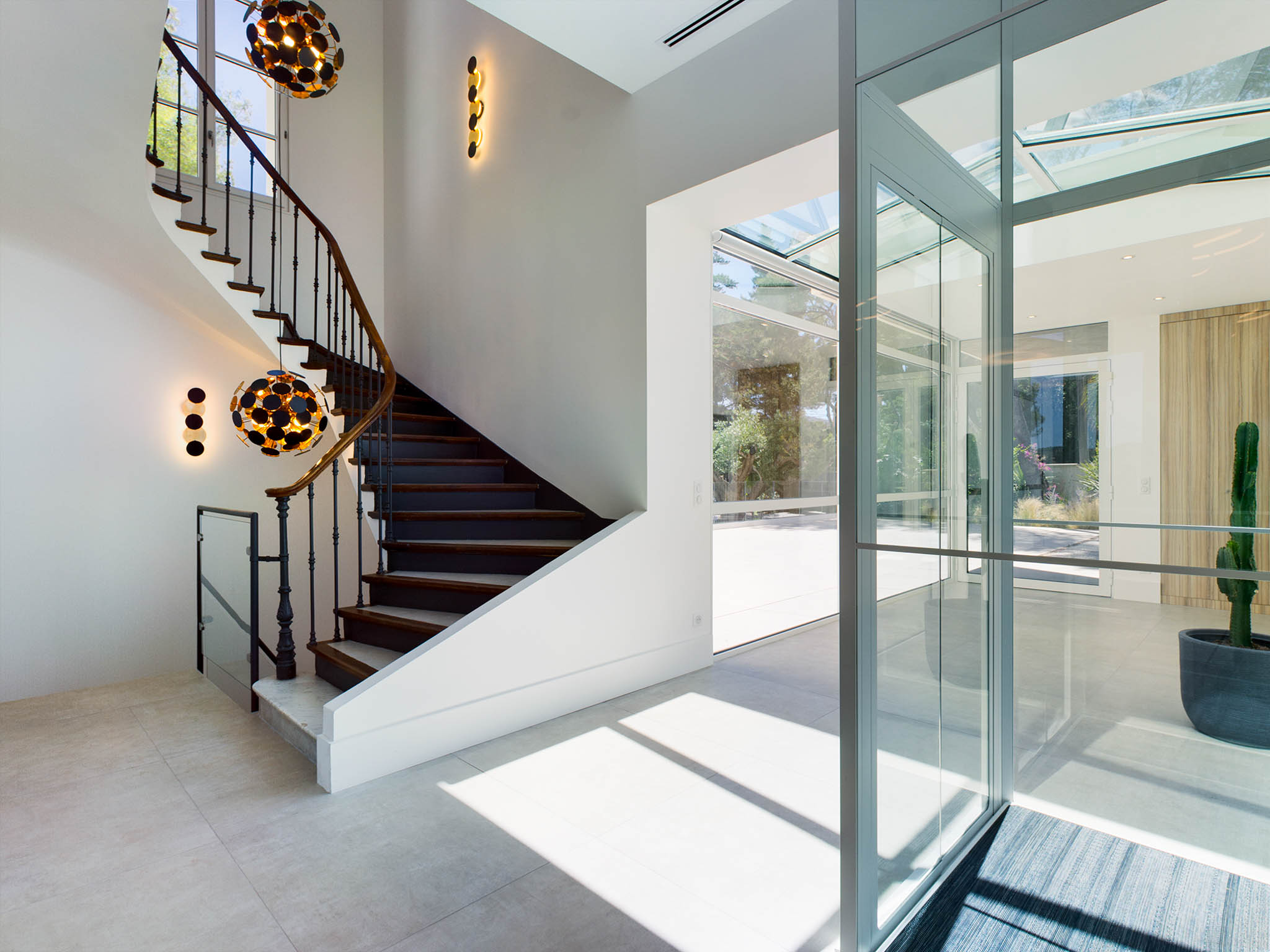 Contemporary venue entrance hall with curved walnut staircase, gold pendant lights, and floor-to-ceiling glass partition