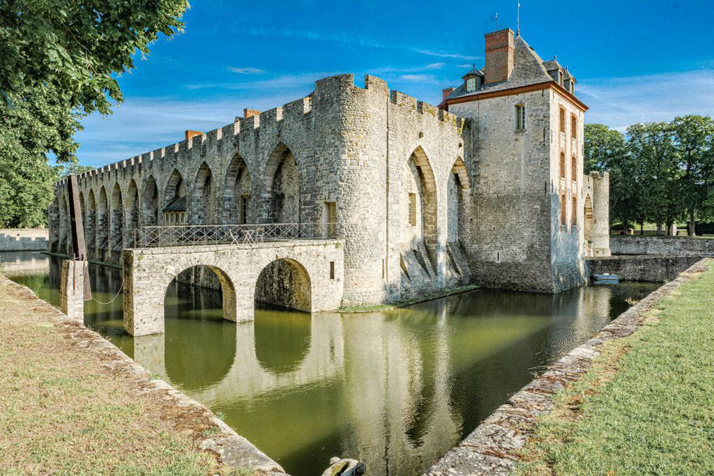 Medieval French chateau with crenellated towers surrounded by a water-filled moat and stone bridge