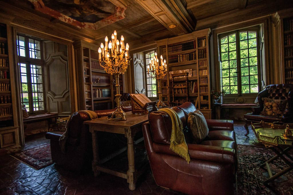 Chateau library with burgundy leather armchairs, floor-to-ceiling bookshelves, and gold candelabra lamps