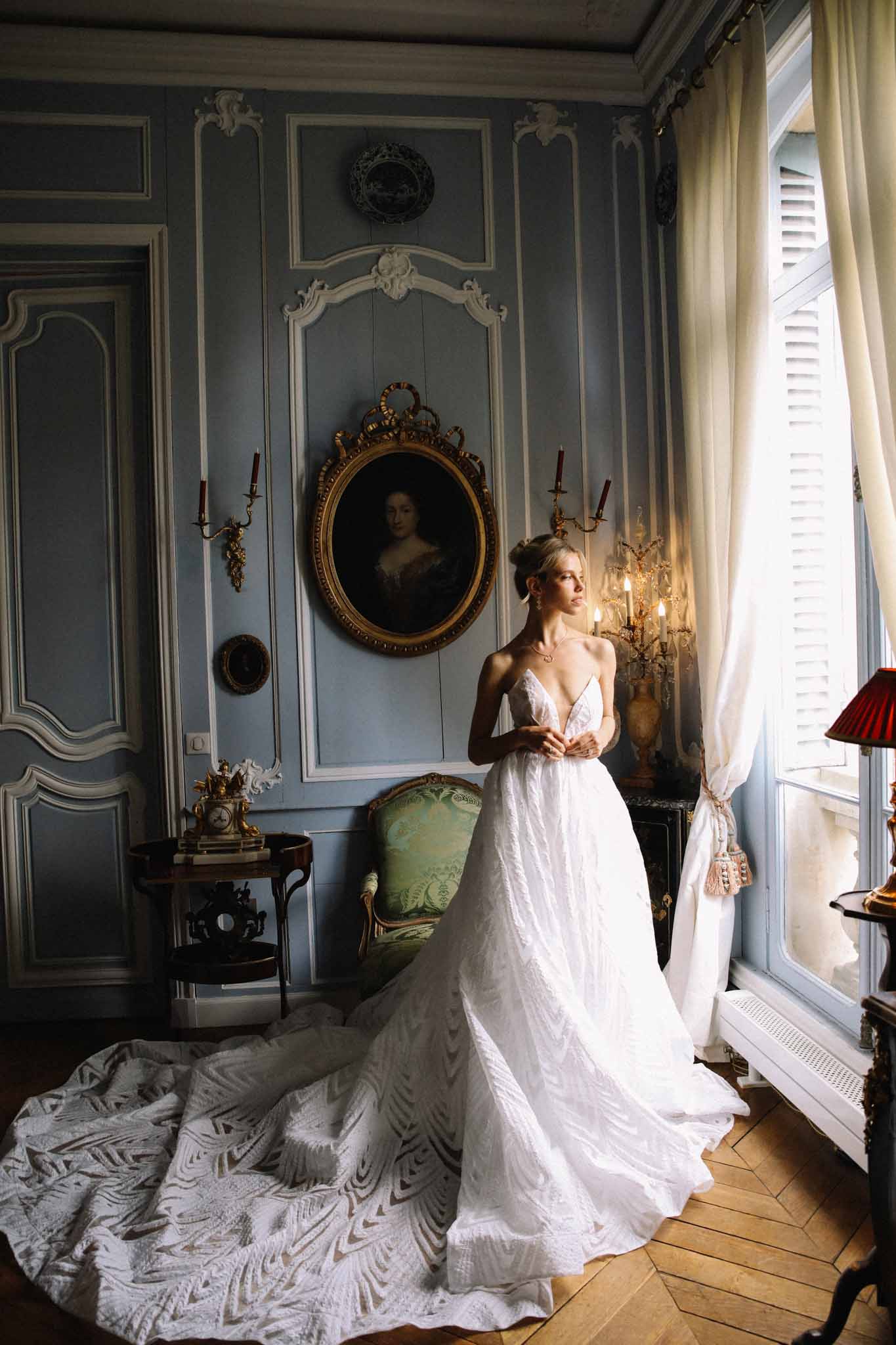 Bride in lace V-neck gown with cathedral train standing in a chateau room with parquet floors and boiserie