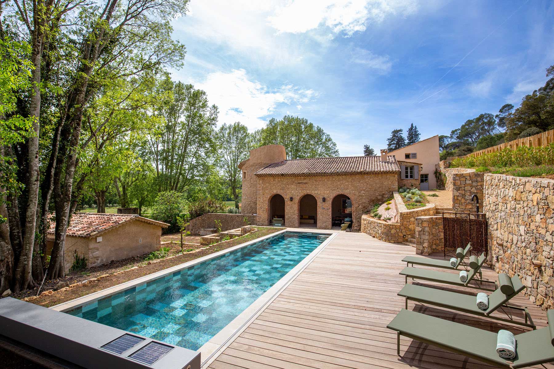 Provencal stone mas with arched pool house, turquoise lap pool, wood deck, and olive-green sun loungers
