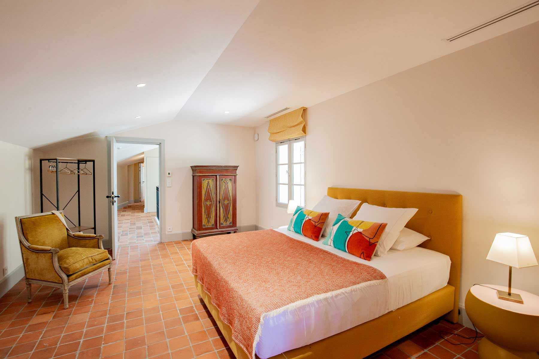 Guest bedroom with mustard headboard, terracotta tile floor, and painted armoire in a Provencal venue