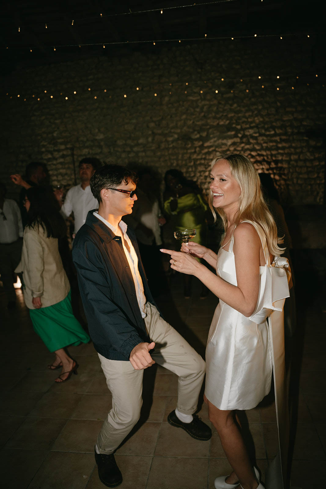 Wedding guests mingling with cocktails at indoor reception with string lights