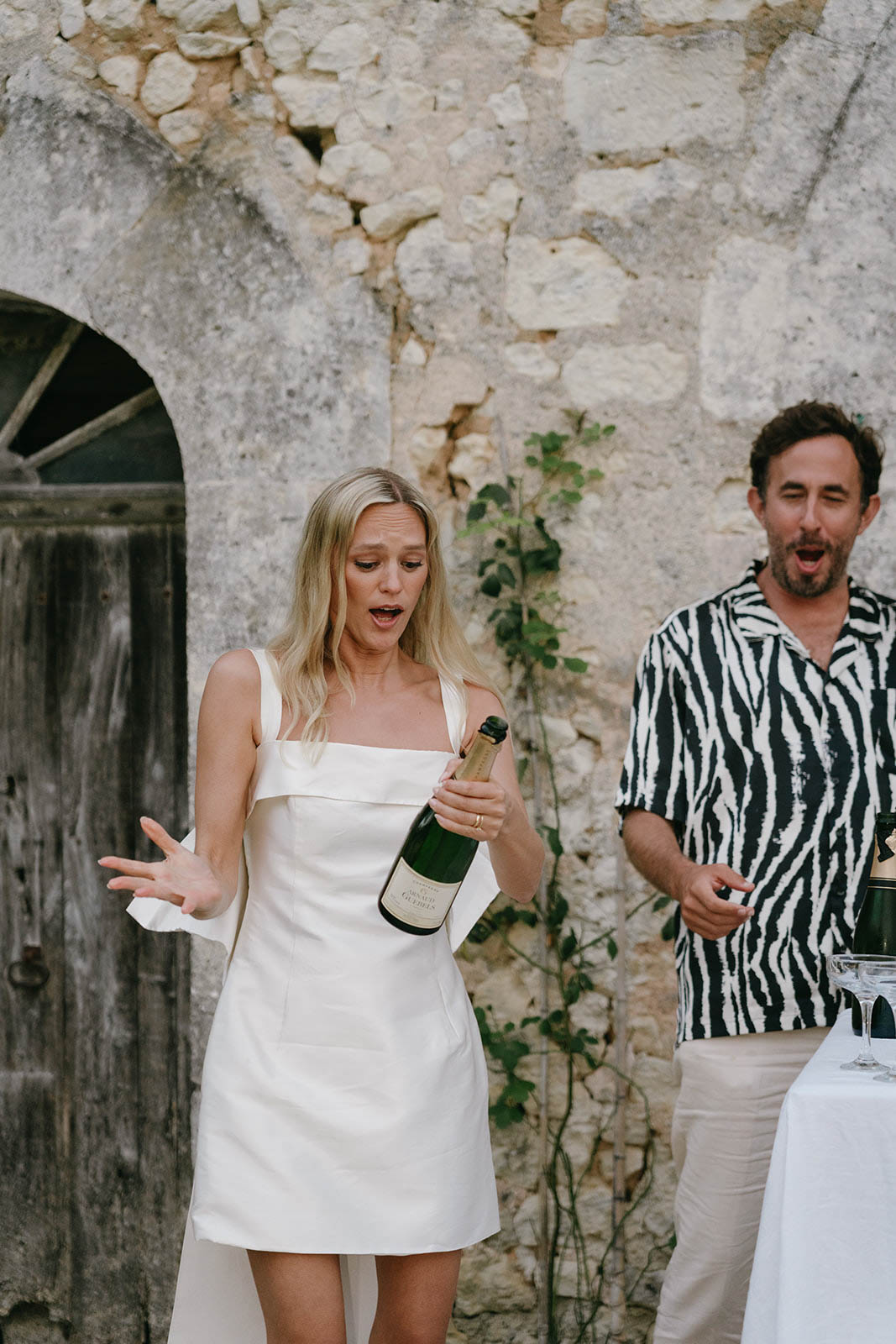 Bride giving toast with champagne bottle during reception celebration in rustic courtyard