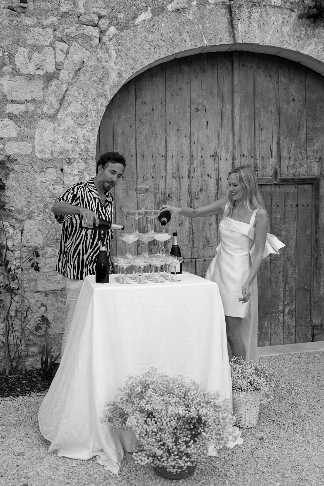 Couple pouring champagne at outdoor reception in Mediterranean courtyard setting