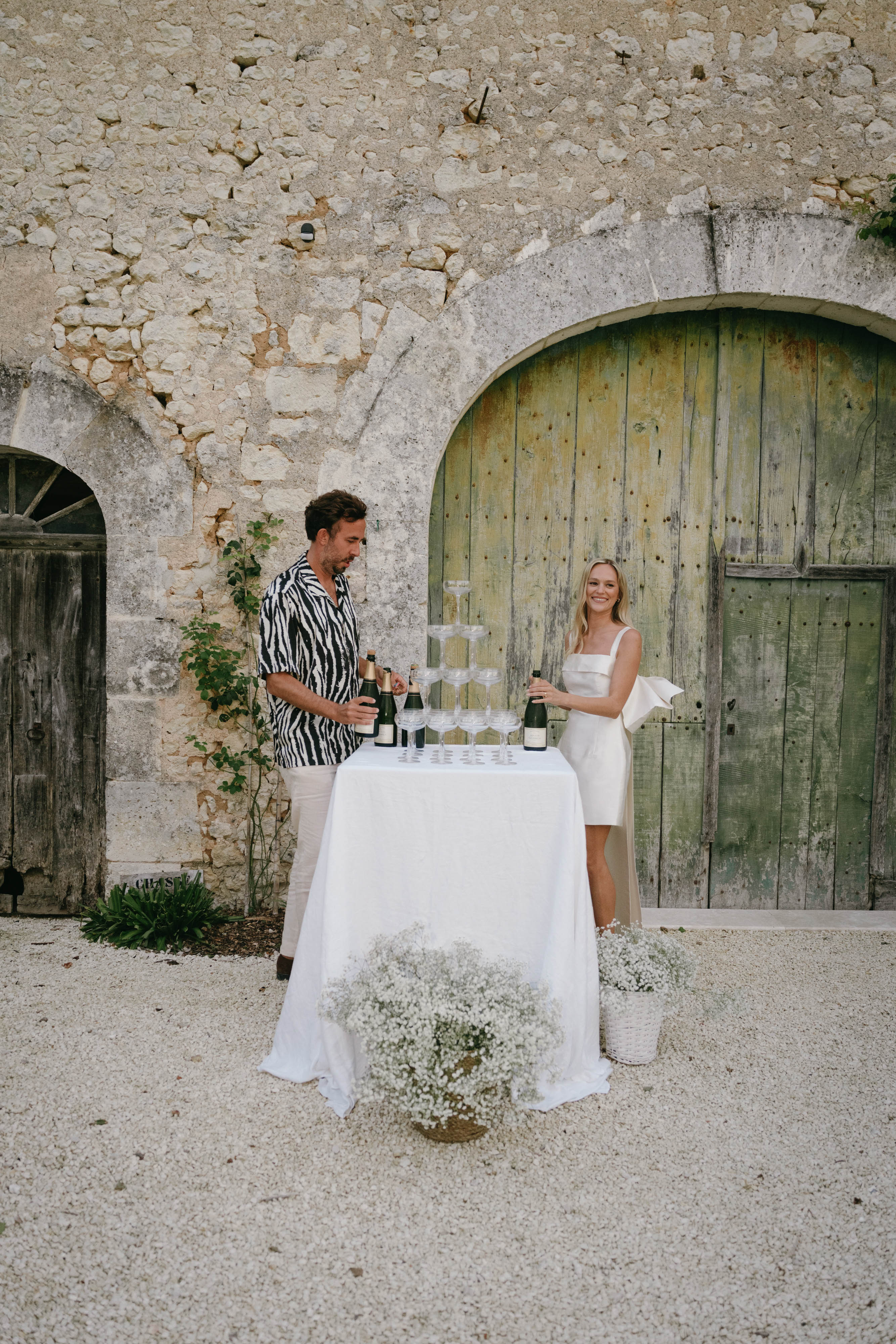 Couple at cocktail hour wine station in historic stone courtyard with arched wooden doors