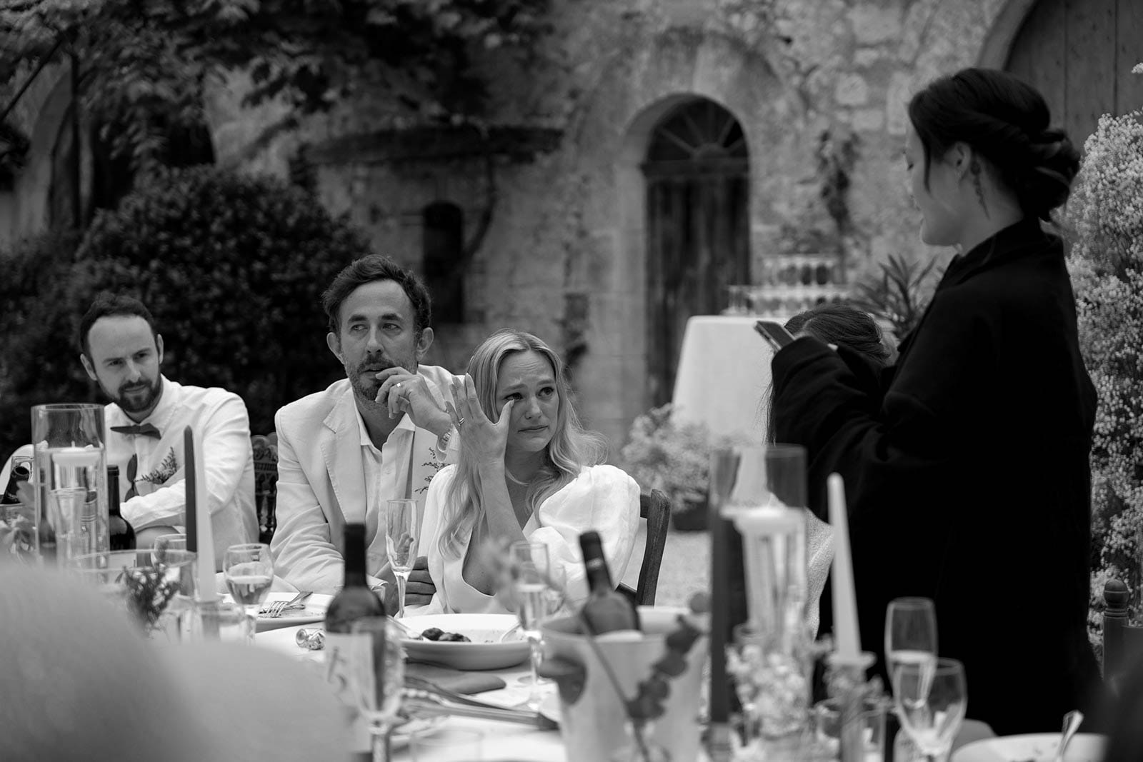 Wedding reception speech moment at outdoor dining table with historic stone building backdrop