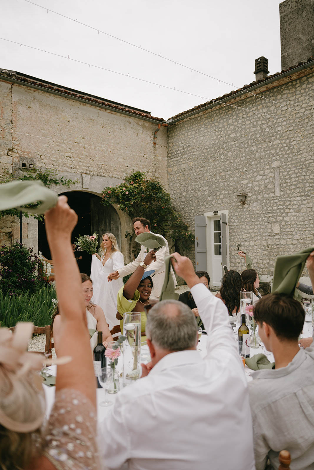 Wedding reception celebration in stone courtyard with guests waving napkins at couple