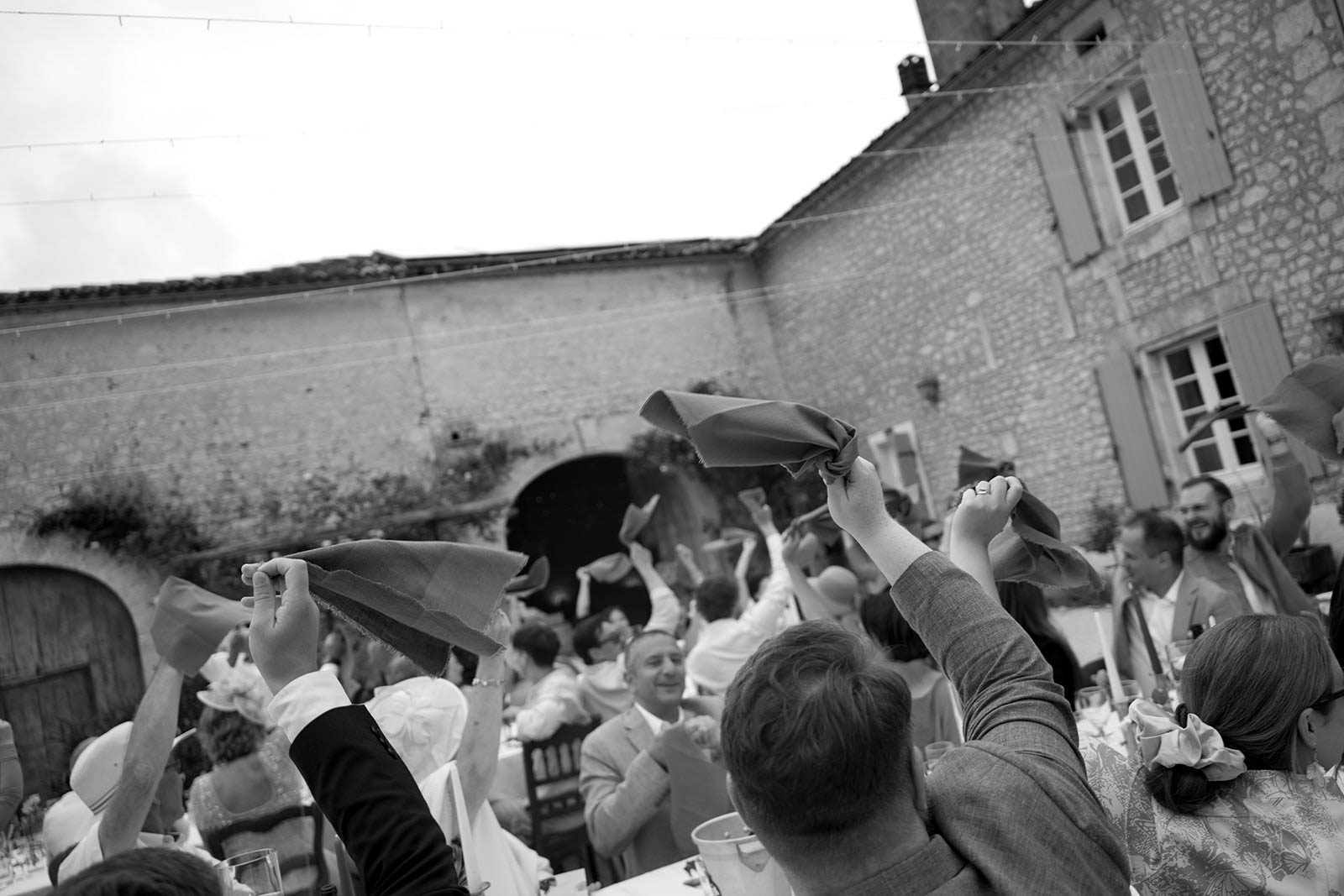 Wedding guests raising napkins in celebratory toast at outdoor courtyard reception