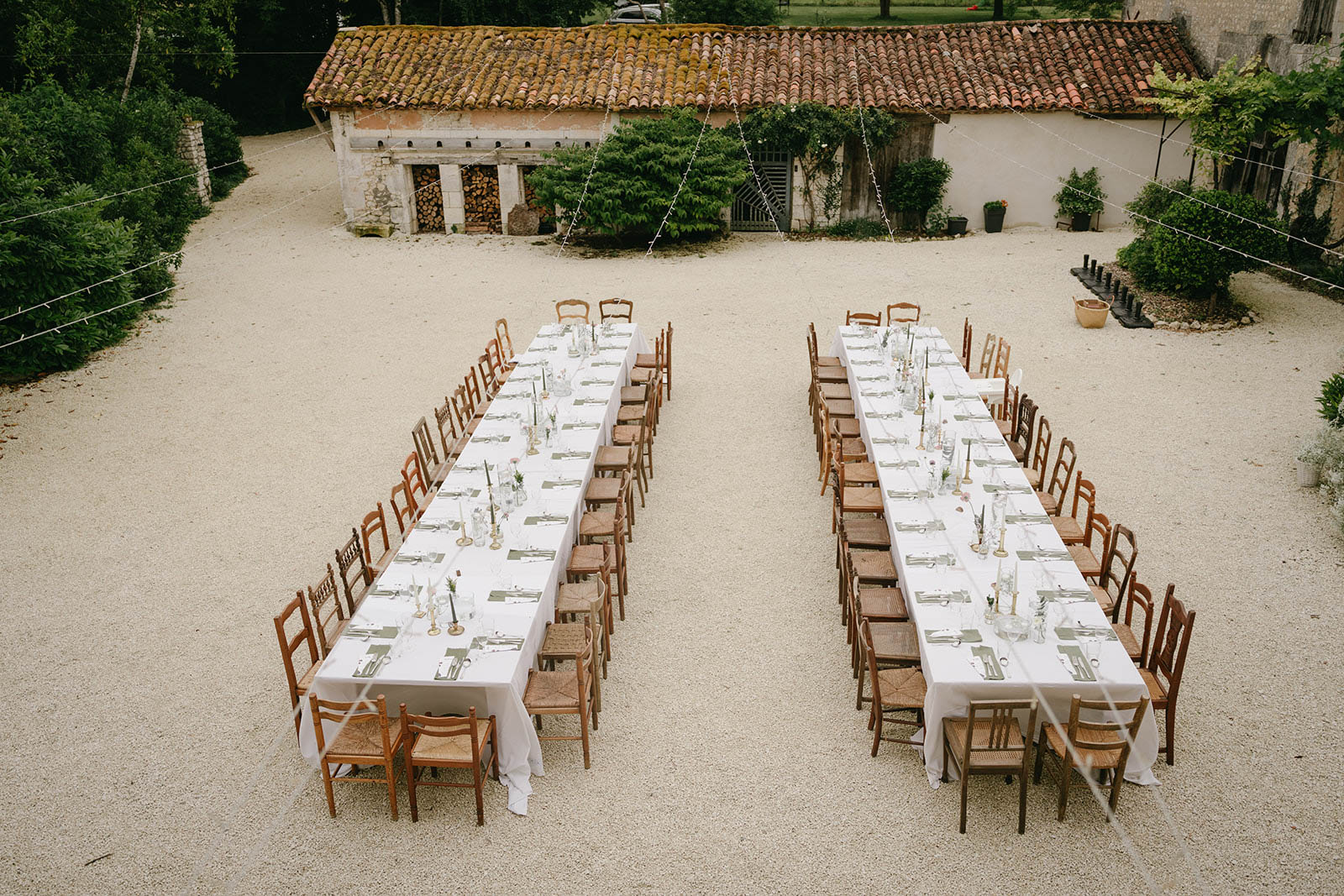Aerial view of rustic courtyard reception setup with long banquet tables at French countryside venue