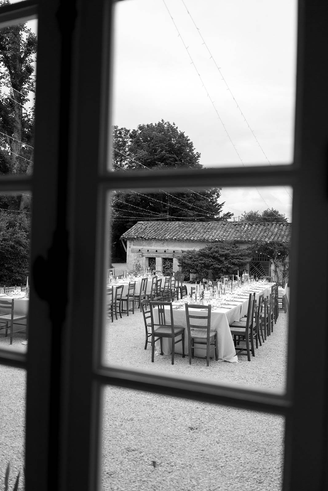 Black and white reception setup in stone courtyard venue viewed through window frame