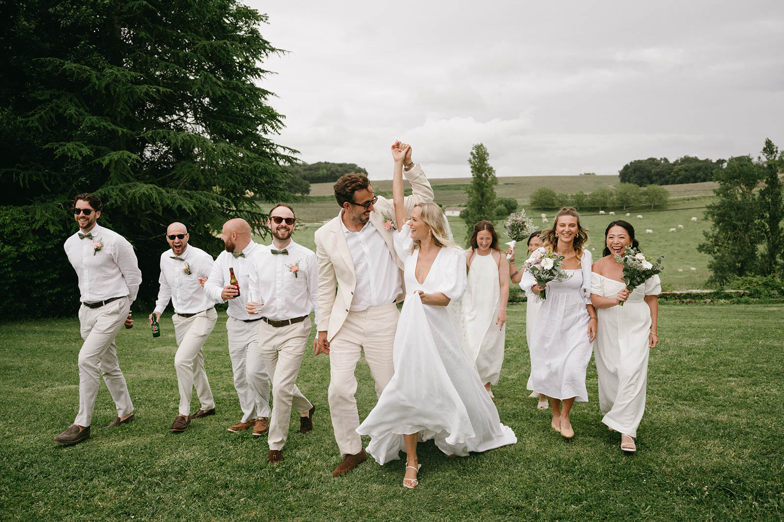 Bride, groom and wedding party celebrating on countryside lawn with rolling hills in background