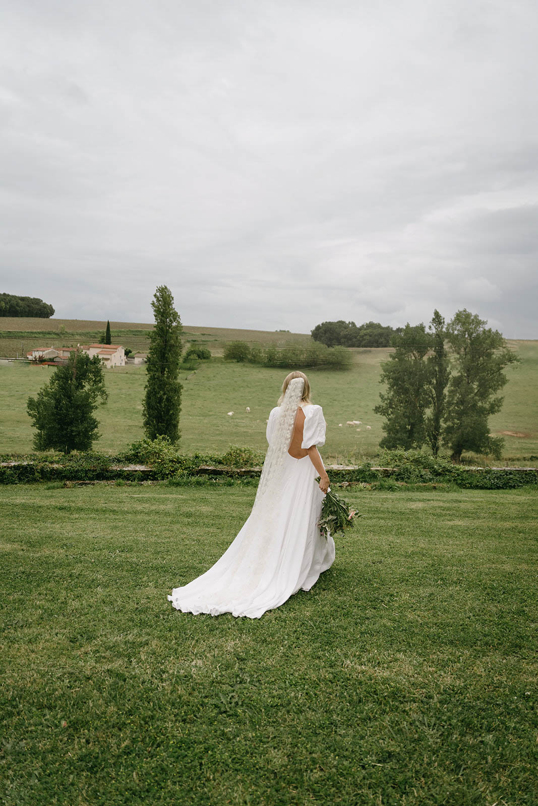 Bride in flowing ivory gown walking across countryside lawn at rural Tuscan farmhouse venue