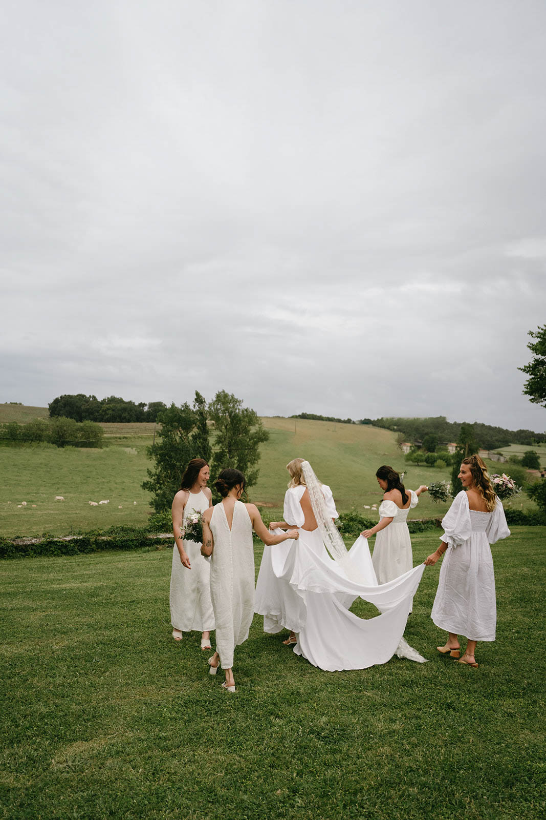 Bride and bridesmaids in white dresses posing in rural field with rolling hills