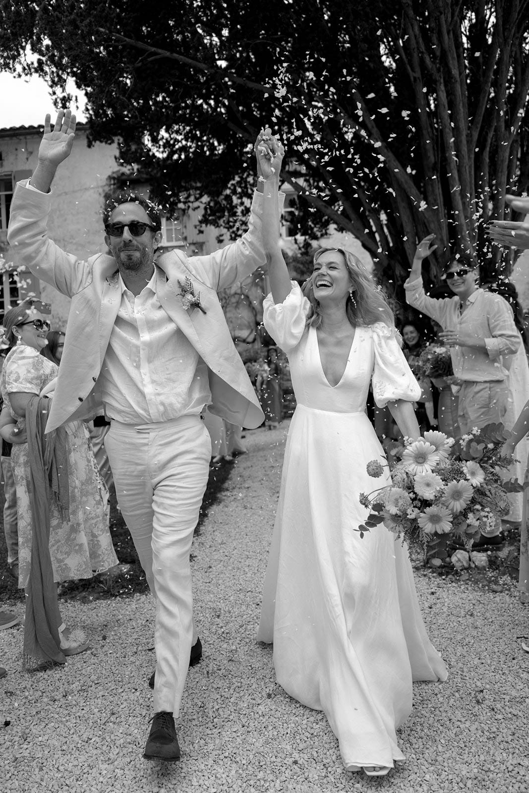 Newlyweds walking down tree-lined pathway after outdoor wedding ceremony with celebrating guests