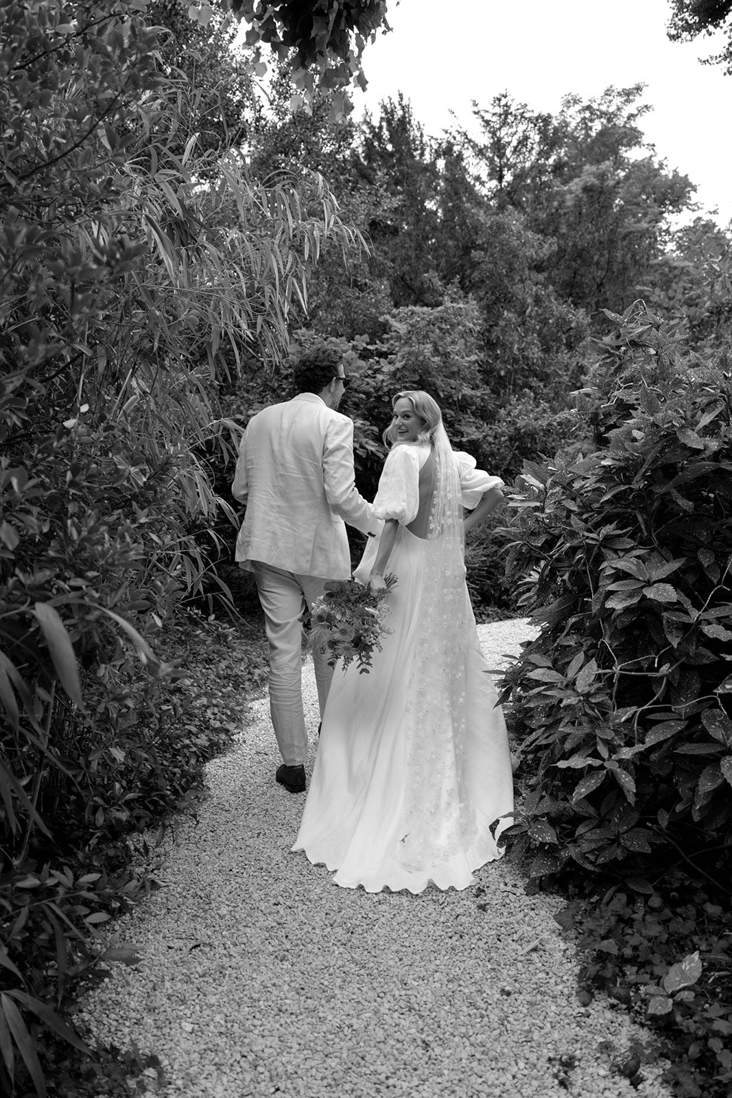 Bride and groom walking together along garden pathway at outdoor wedding venue