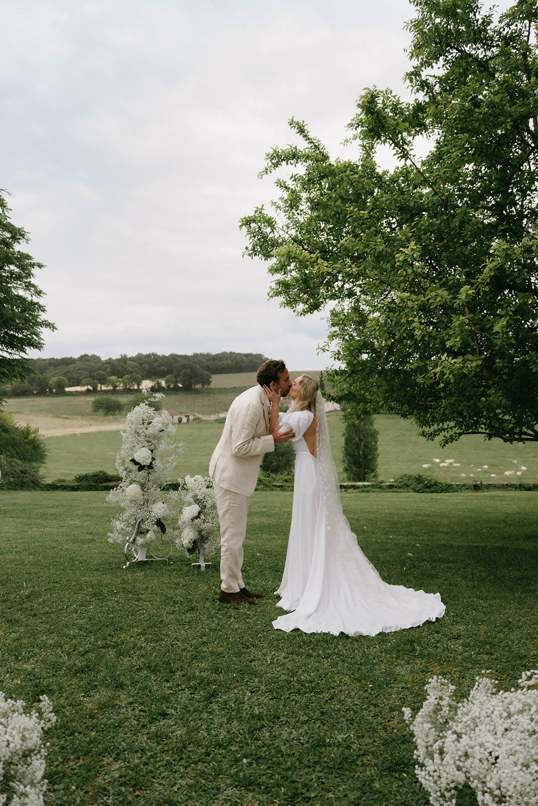 Groom dips and kisses bride during outdoor garden ceremony with countryside views