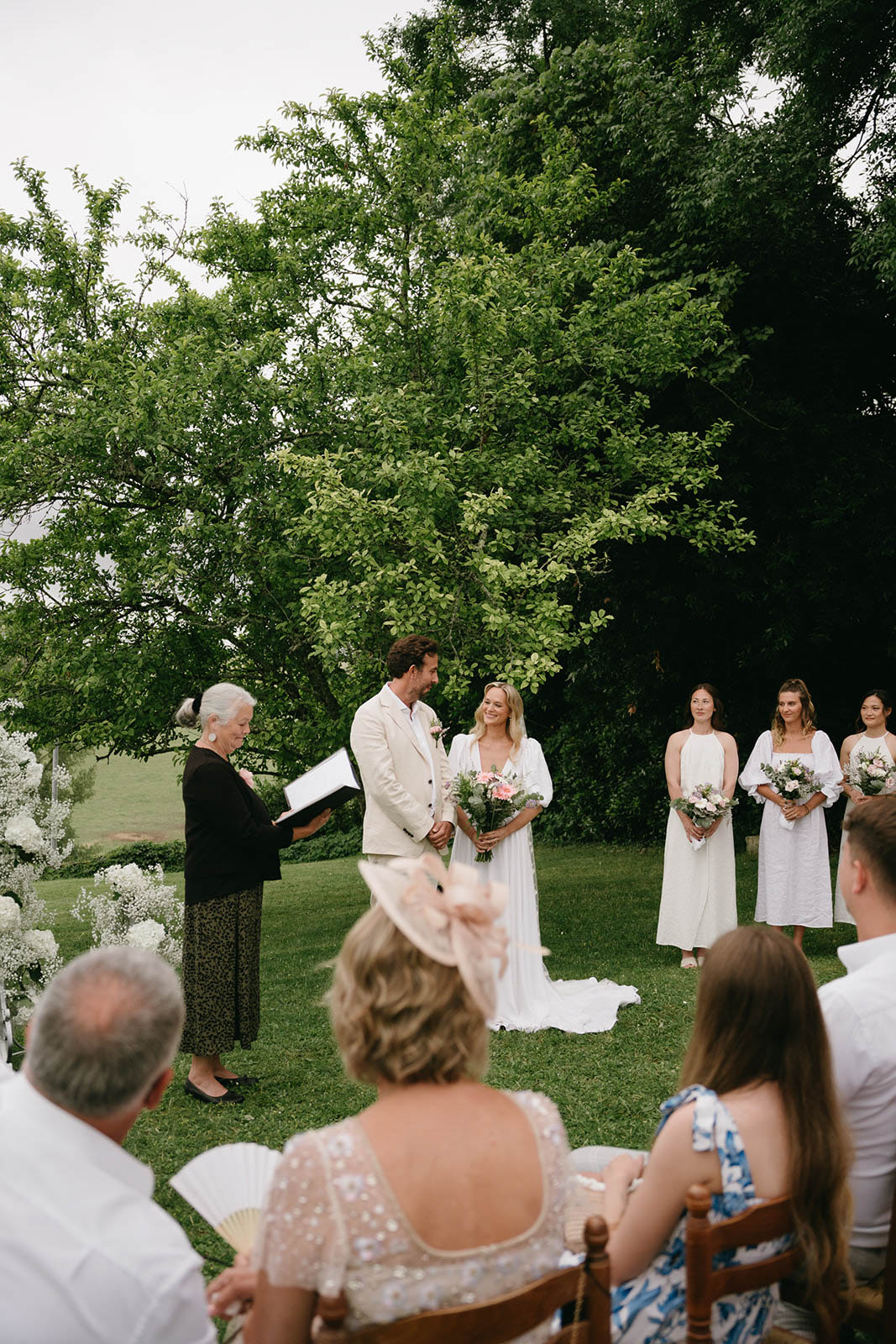 Outdoor wedding ceremony with bride, groom and wedding party in garden setting with white floral arrangements
