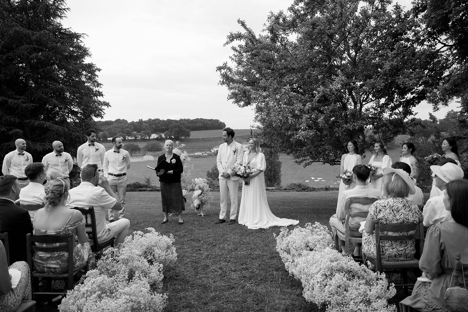Outdoor wedding ceremony in open field with rolling hills and guests seated on chairs