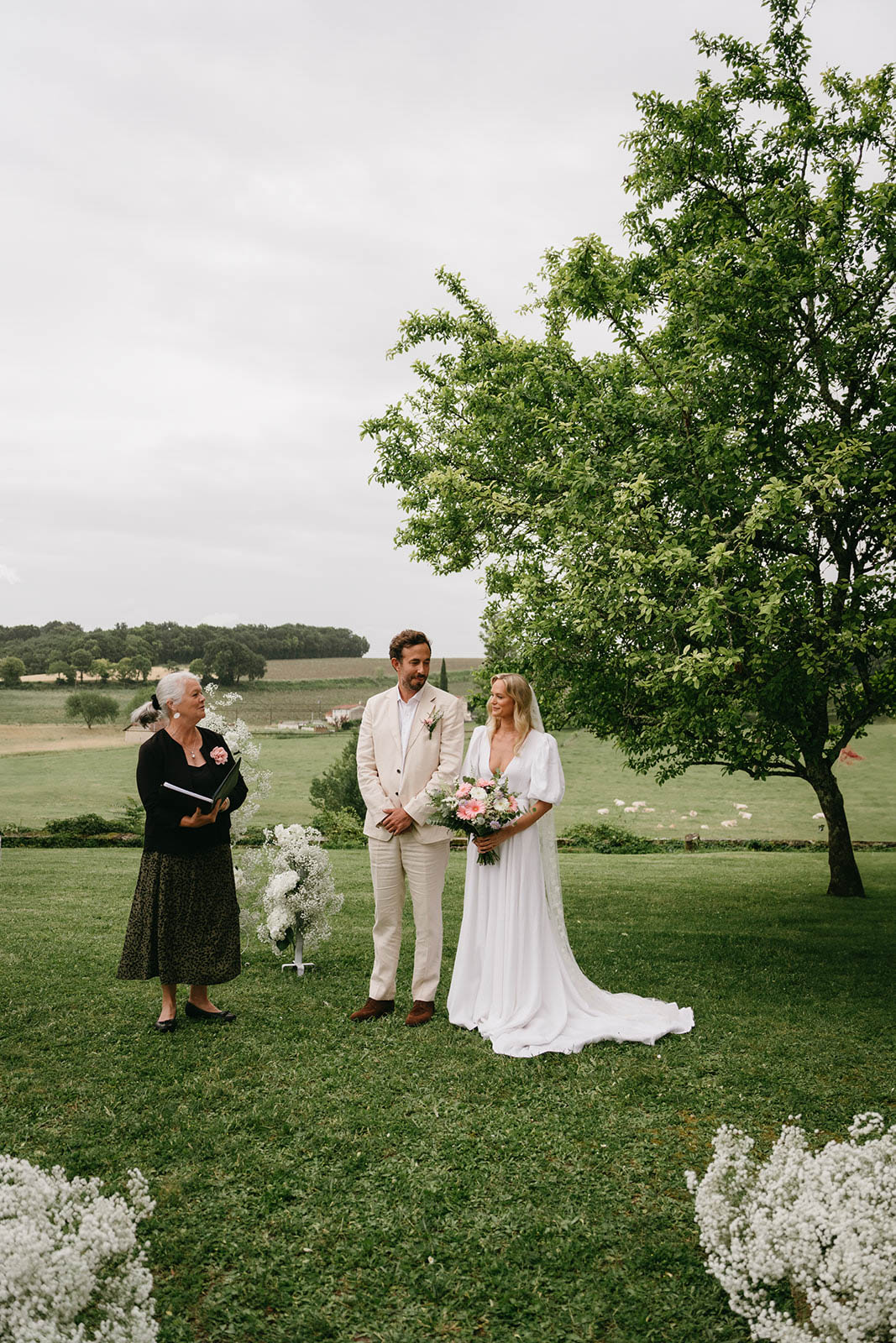 Bride and groom exchanging vows with officiant during outdoor countryside wedding ceremony