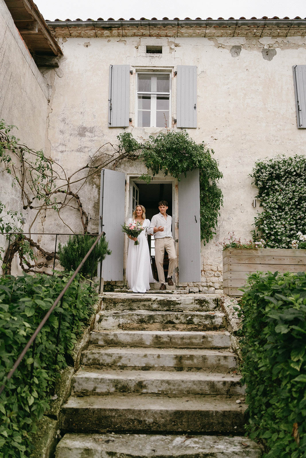 Bride and groom standing in doorway of rustic stone cottage with ivy and weathered shutters