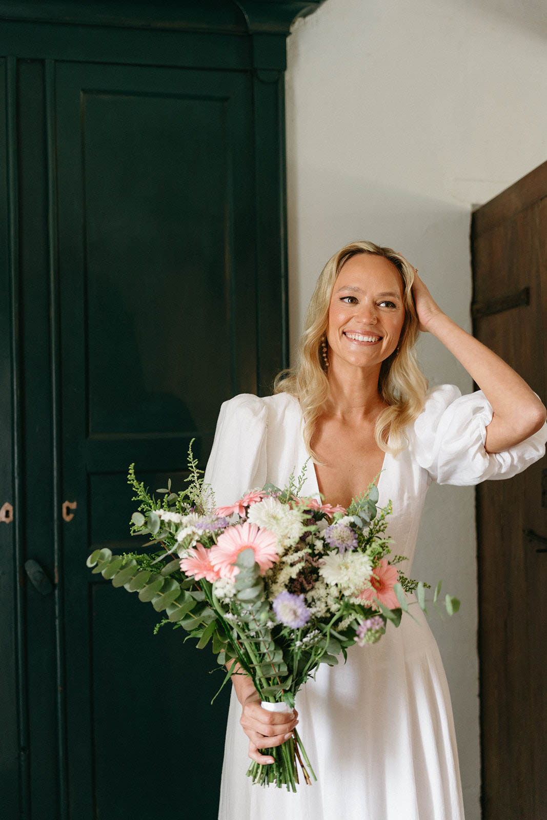 Bride in ivory dress holding coral and white bouquet in elegant interior hallway