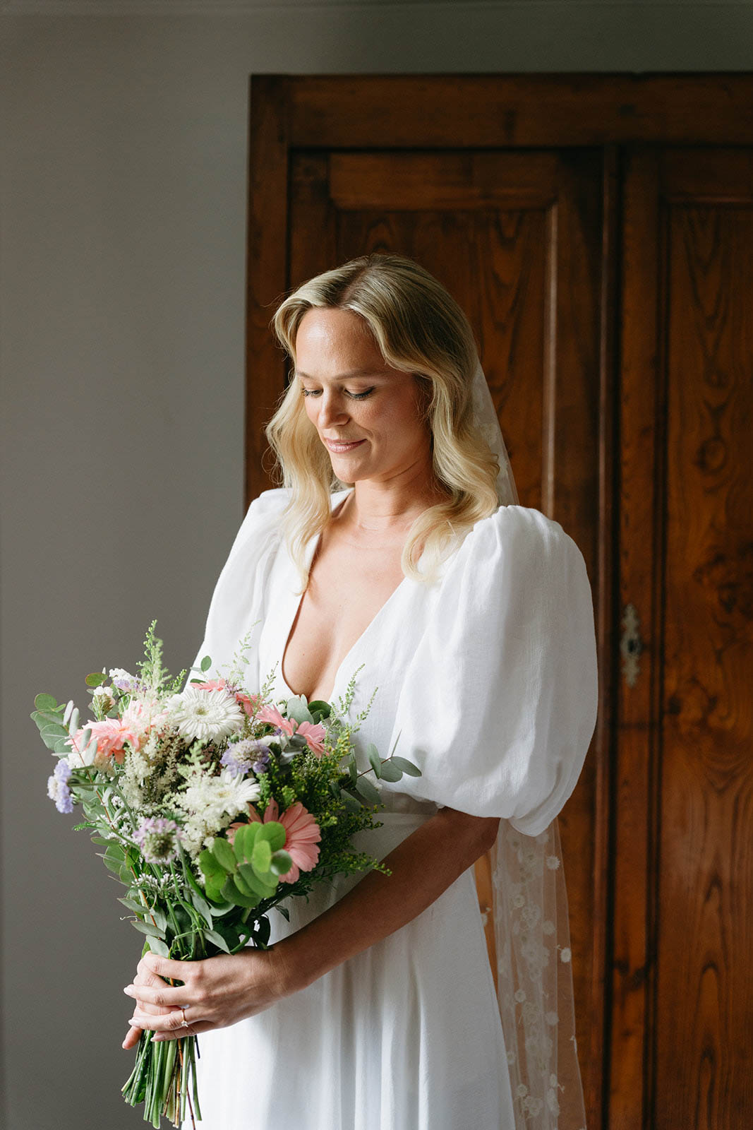 Bride in silk robe holding coral and lavender bouquet indoors