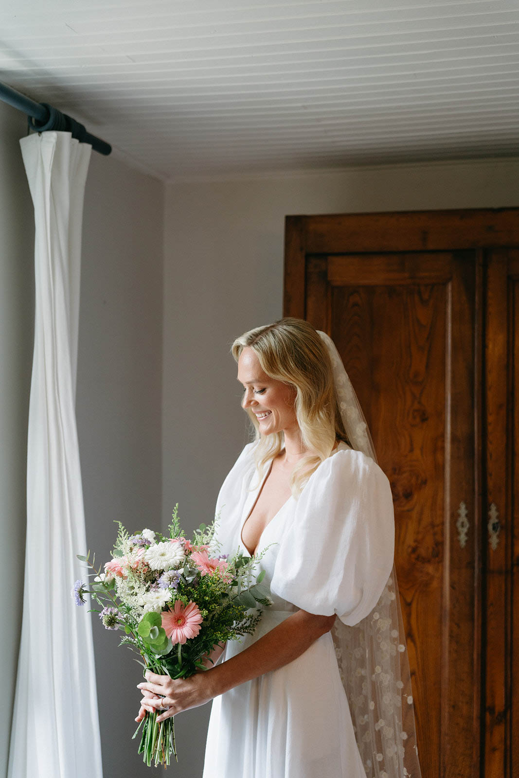 Bride holding bouquet in ivory dress and veil in indoor getting ready space