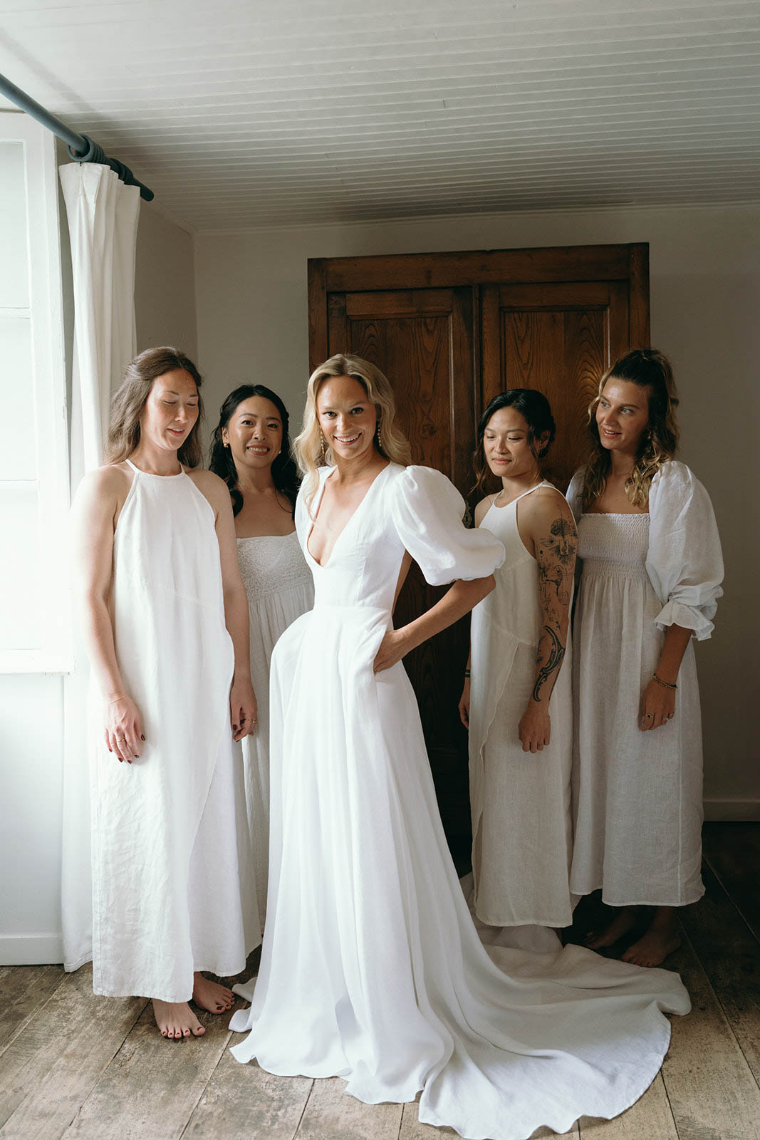 Bride and bridesmaids in neutral dresses posing together in indoor getting-ready room