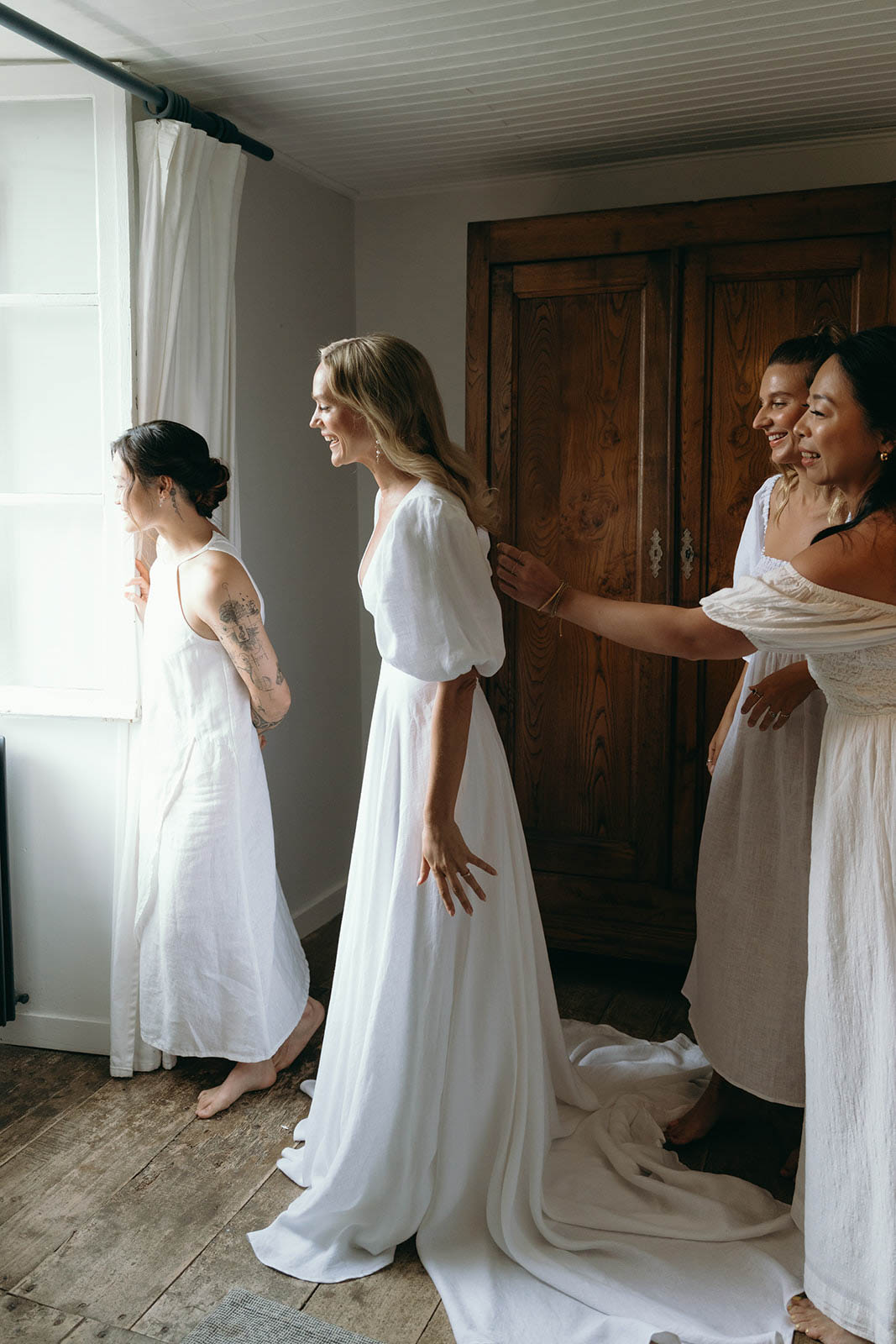 Bride getting ready with three bridesmaids in ivory linen dresses in rustic modern indoor room