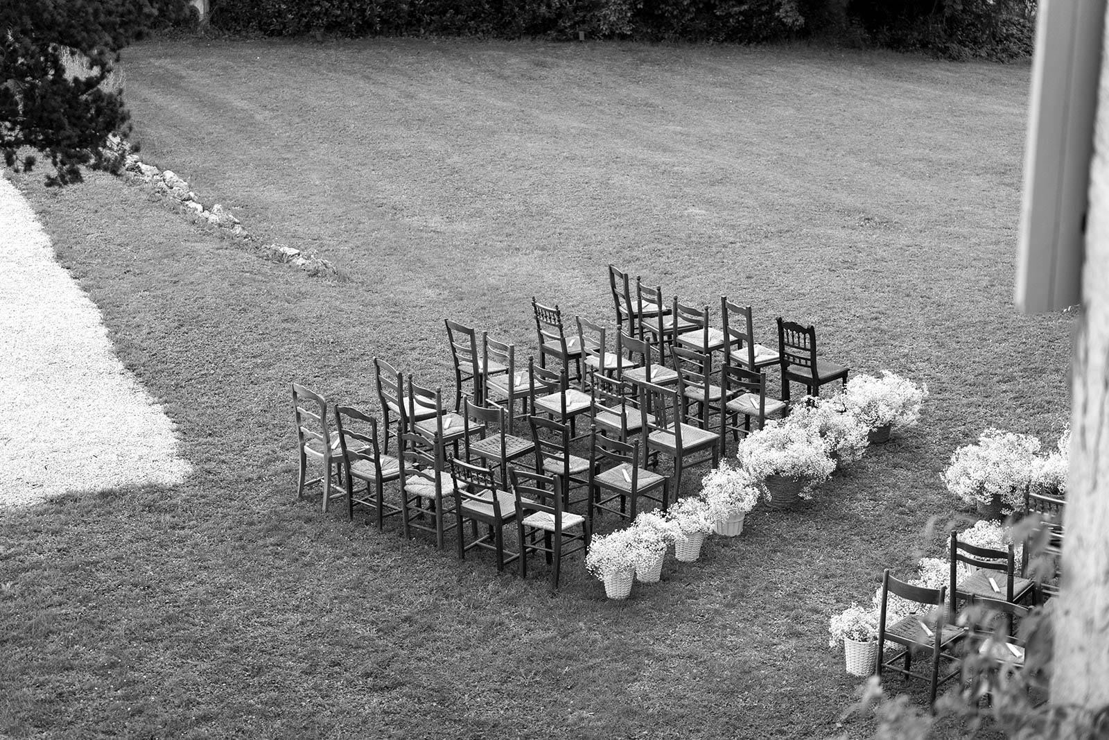 Aerial view of outdoor wedding ceremony setup with wooden chairs and white floral aisle in garden courtyard