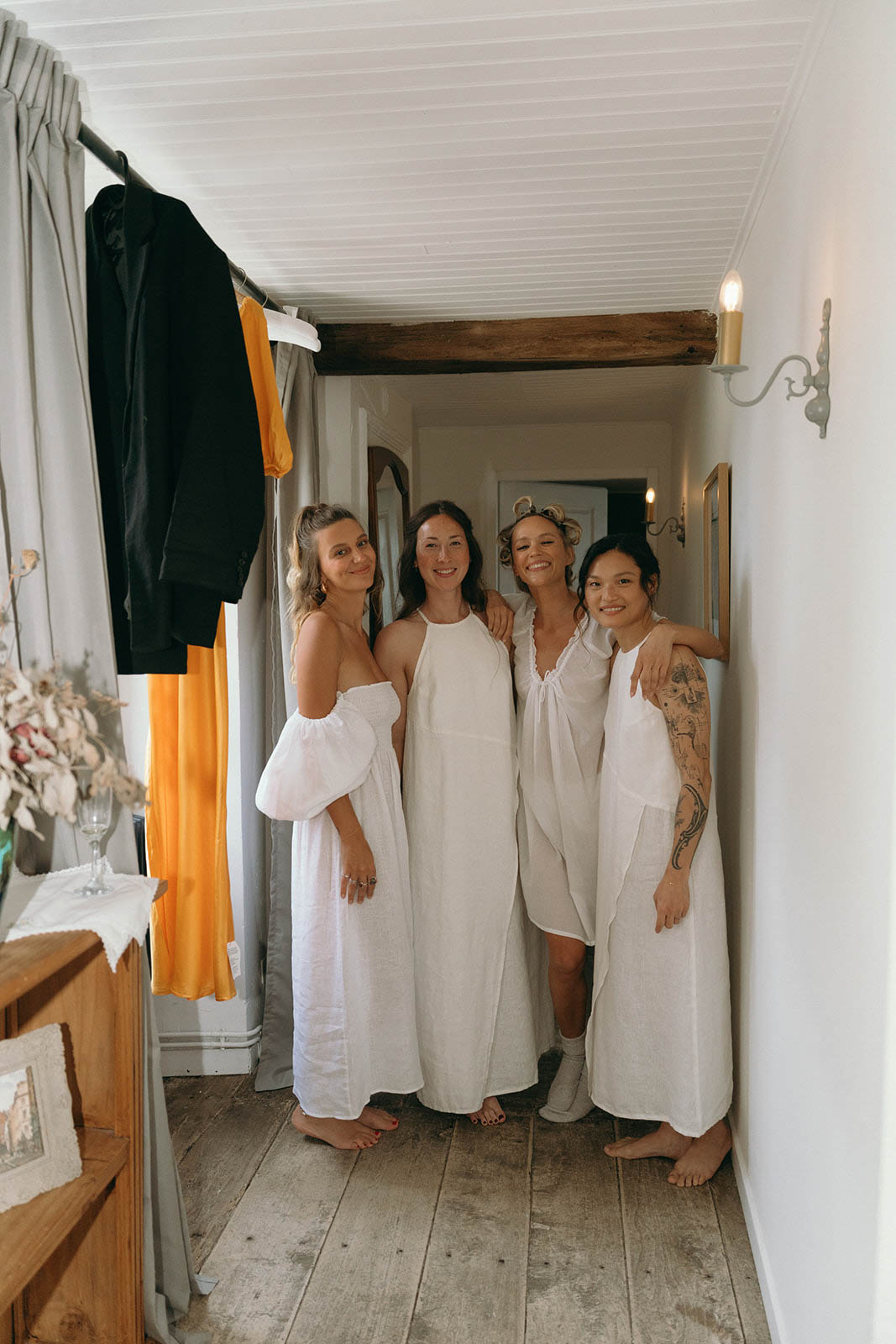 Four bridesmaids in linen robes during getting ready preparations in rustic hallway with exposed beams