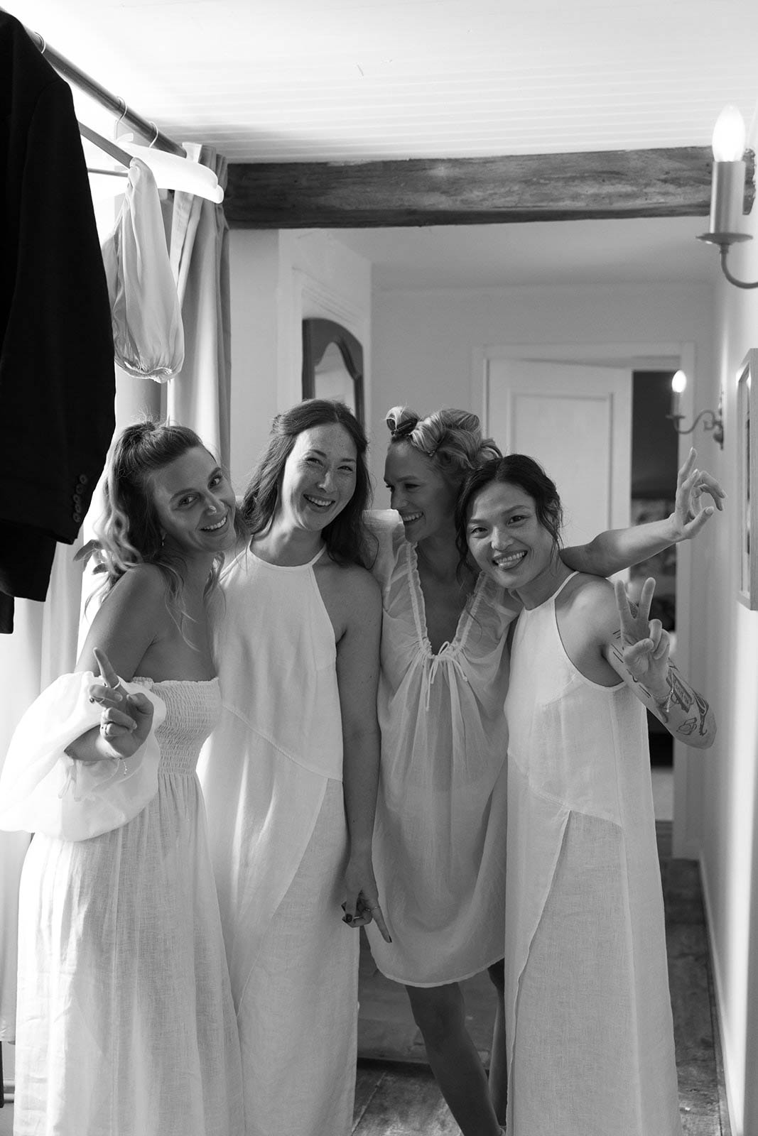 Four bridesmaids in white slip dresses posing together in rustic bedroom during wedding preparation