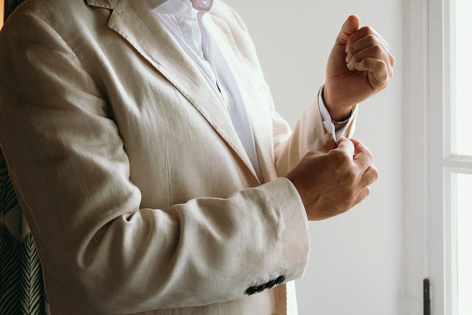 Groom adjusting cufflinks in ivory suit before wedding ceremony