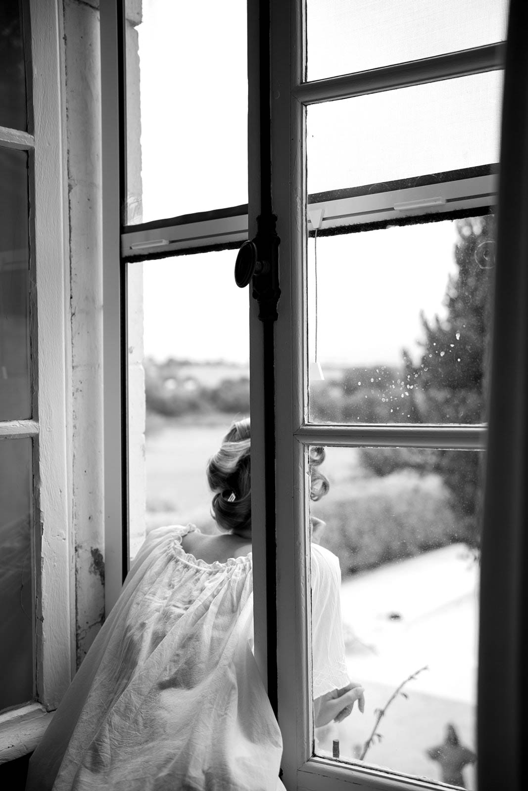 Bride in wedding dress looking out window in contemplative black and white portrait at scenic wedding venue