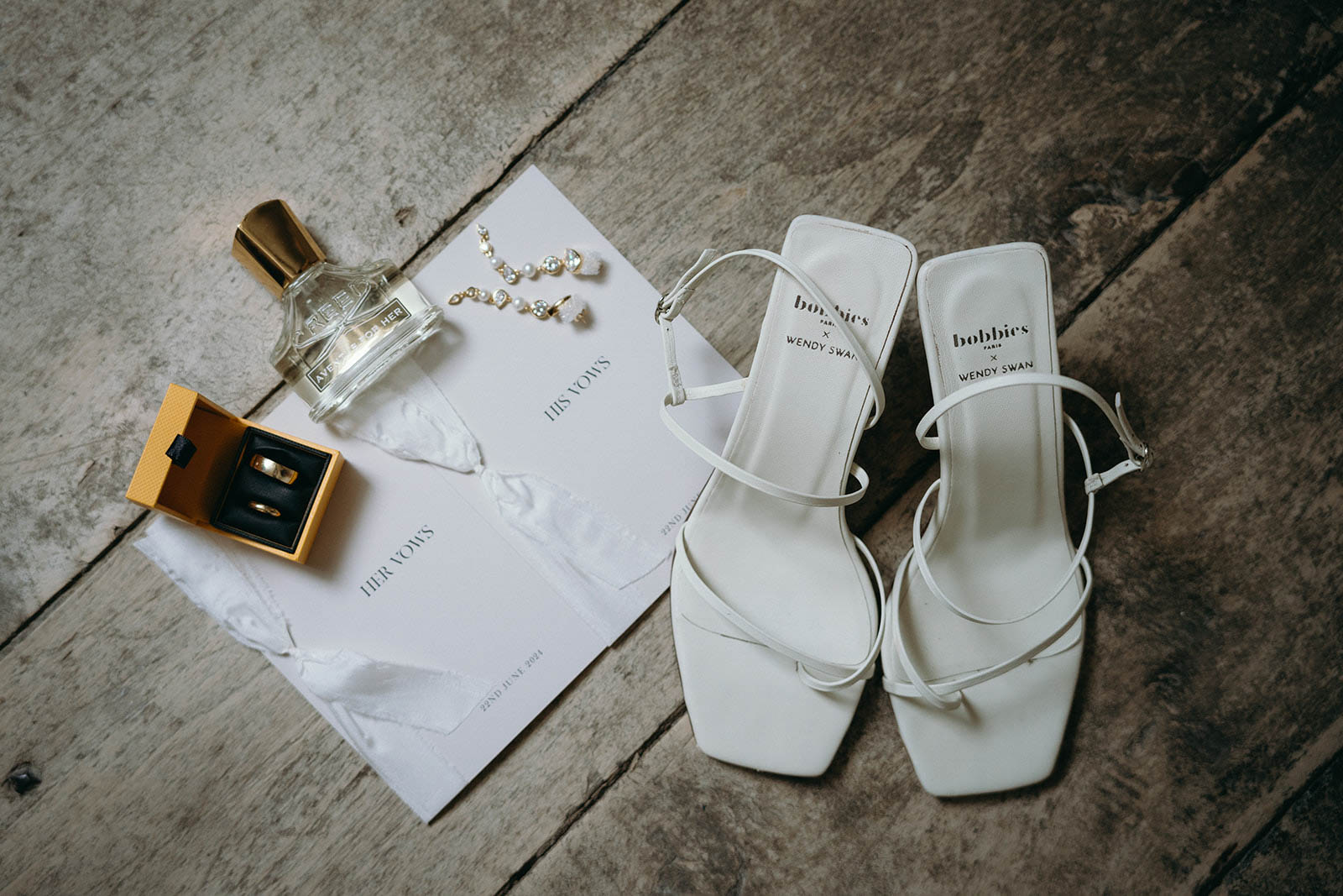 Bridal accessories flat lay with ballet shoes, rings, and ceremony program on weathered wood surface