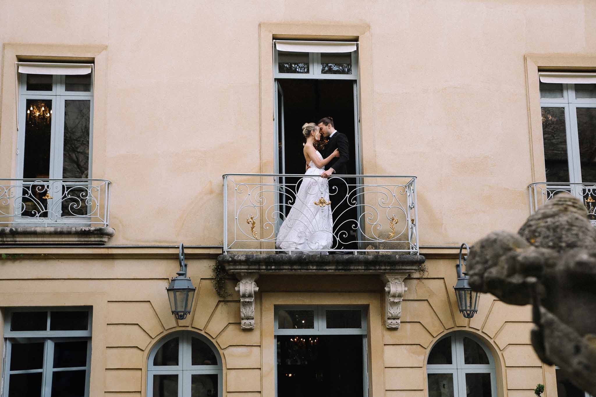 Bride and groom embracing on wrought-iron balcony of classical Haussmann building