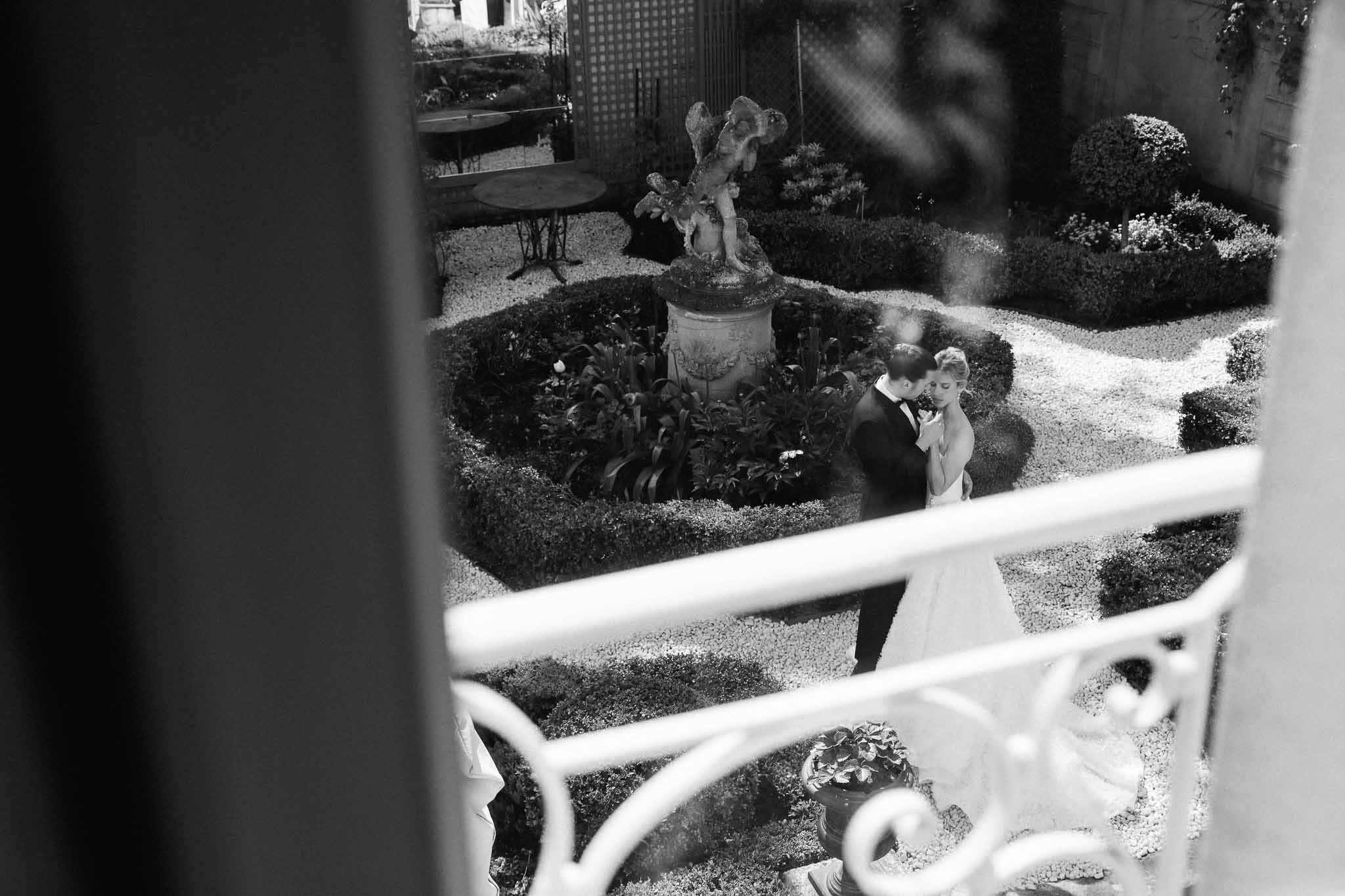 Bride and groom posing in formal garden with classical stone urn and manicured hedging
