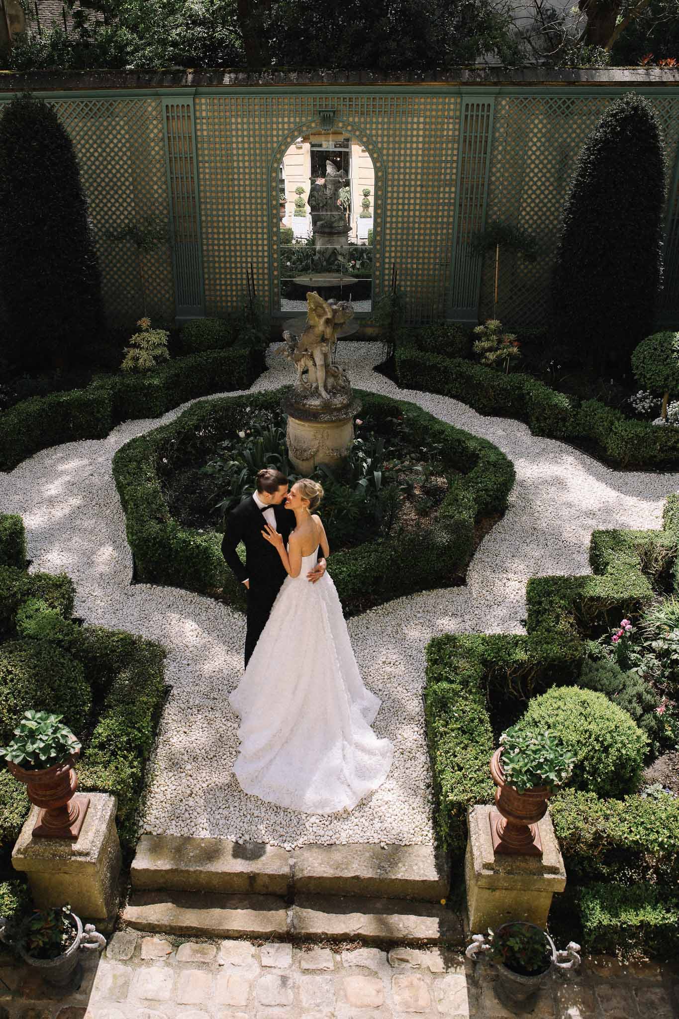 Bride and groom in formal French garden courtyard with geometric hedges and fountain