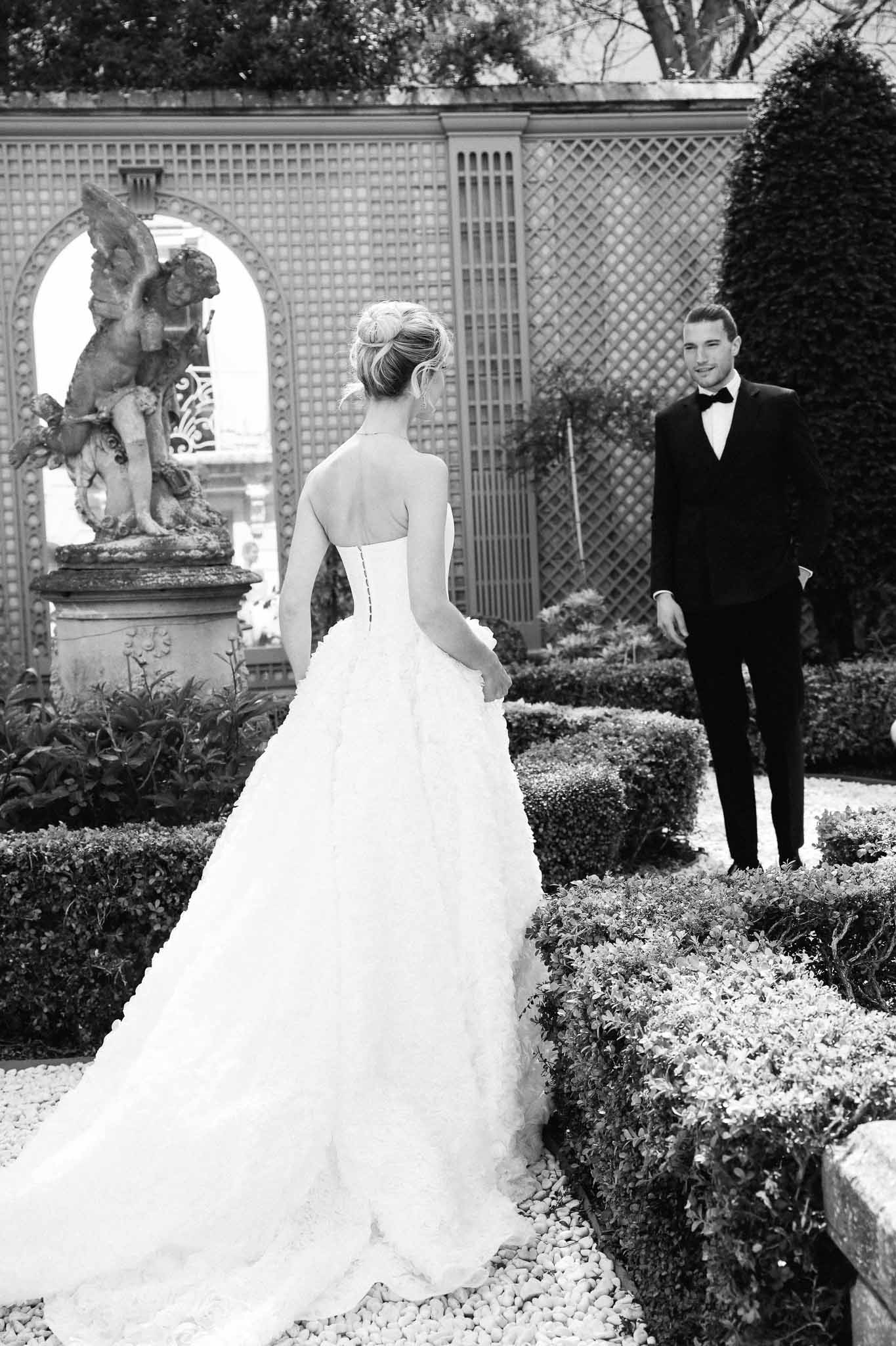 Bride and groom first look moment in formal garden with geometric lattice and stone cherub statue