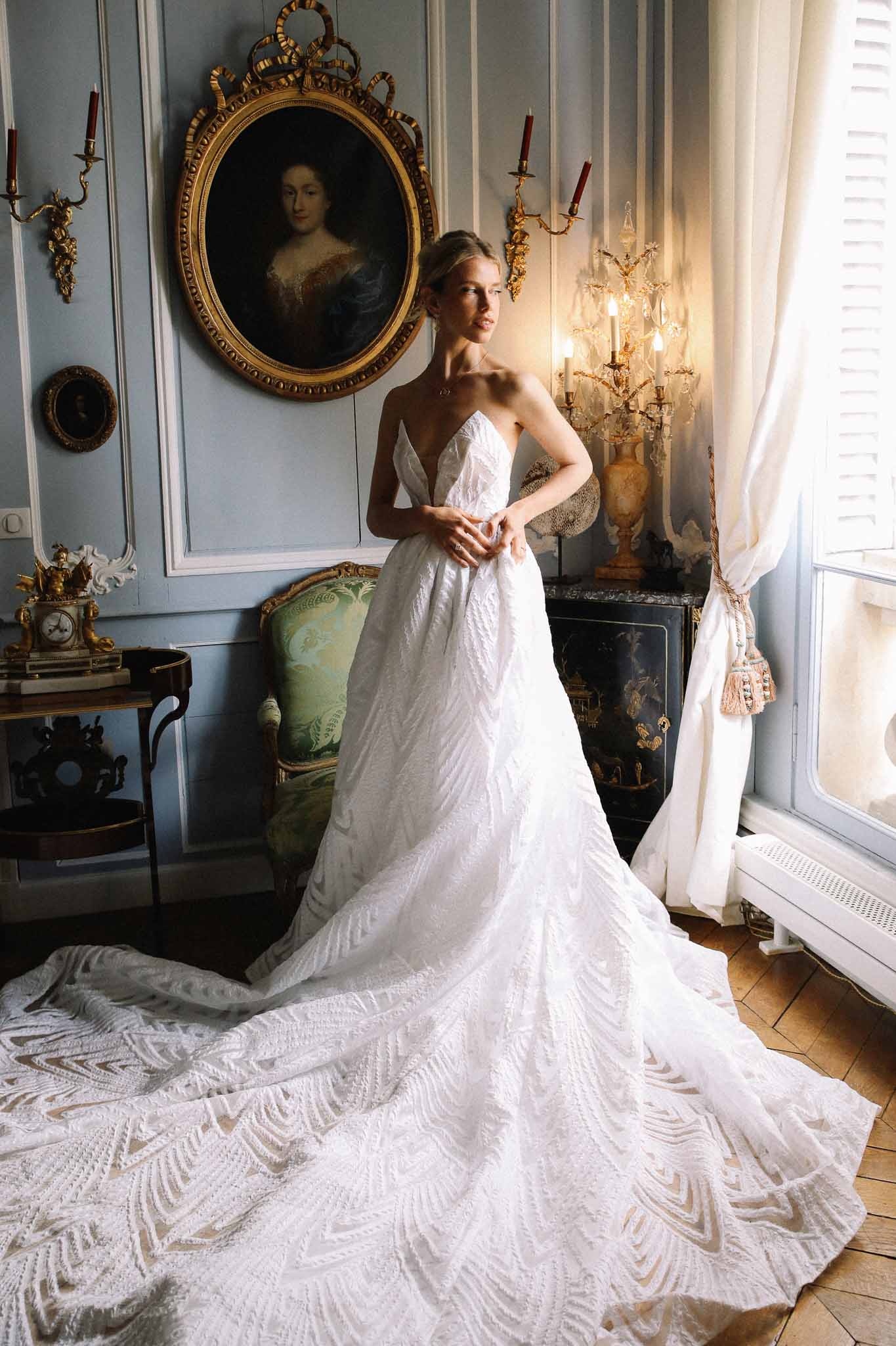 Bride in white strapless gown with geometric train in classical salon with ornate mirrors and antique furniture
