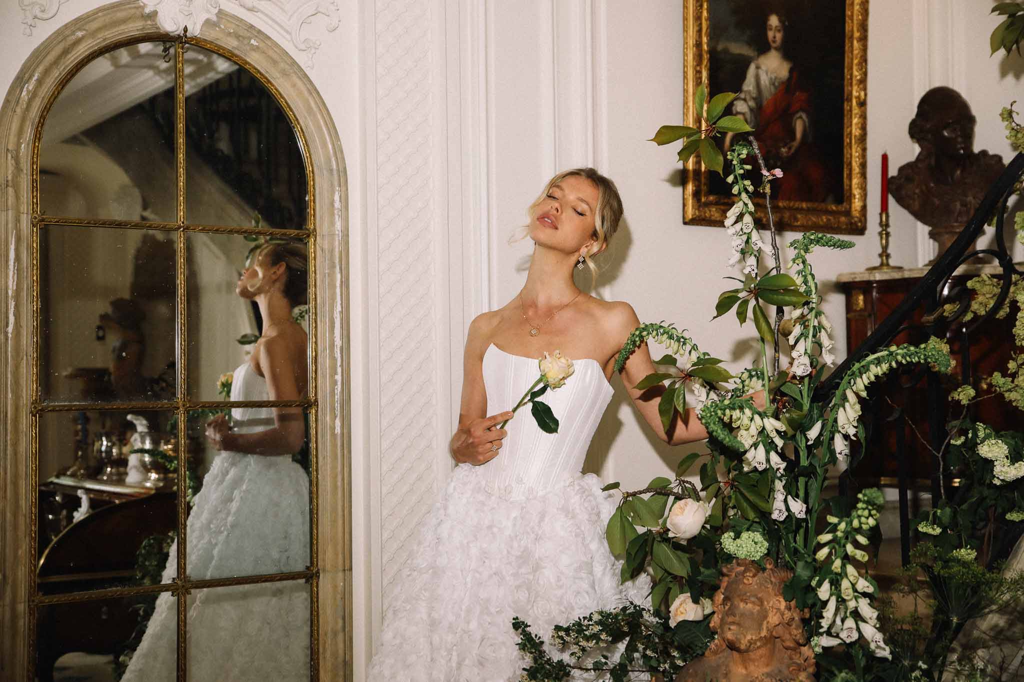 Bride in ivory strapless dress with white floral arrangements in classical interior with gilt frames and mirror