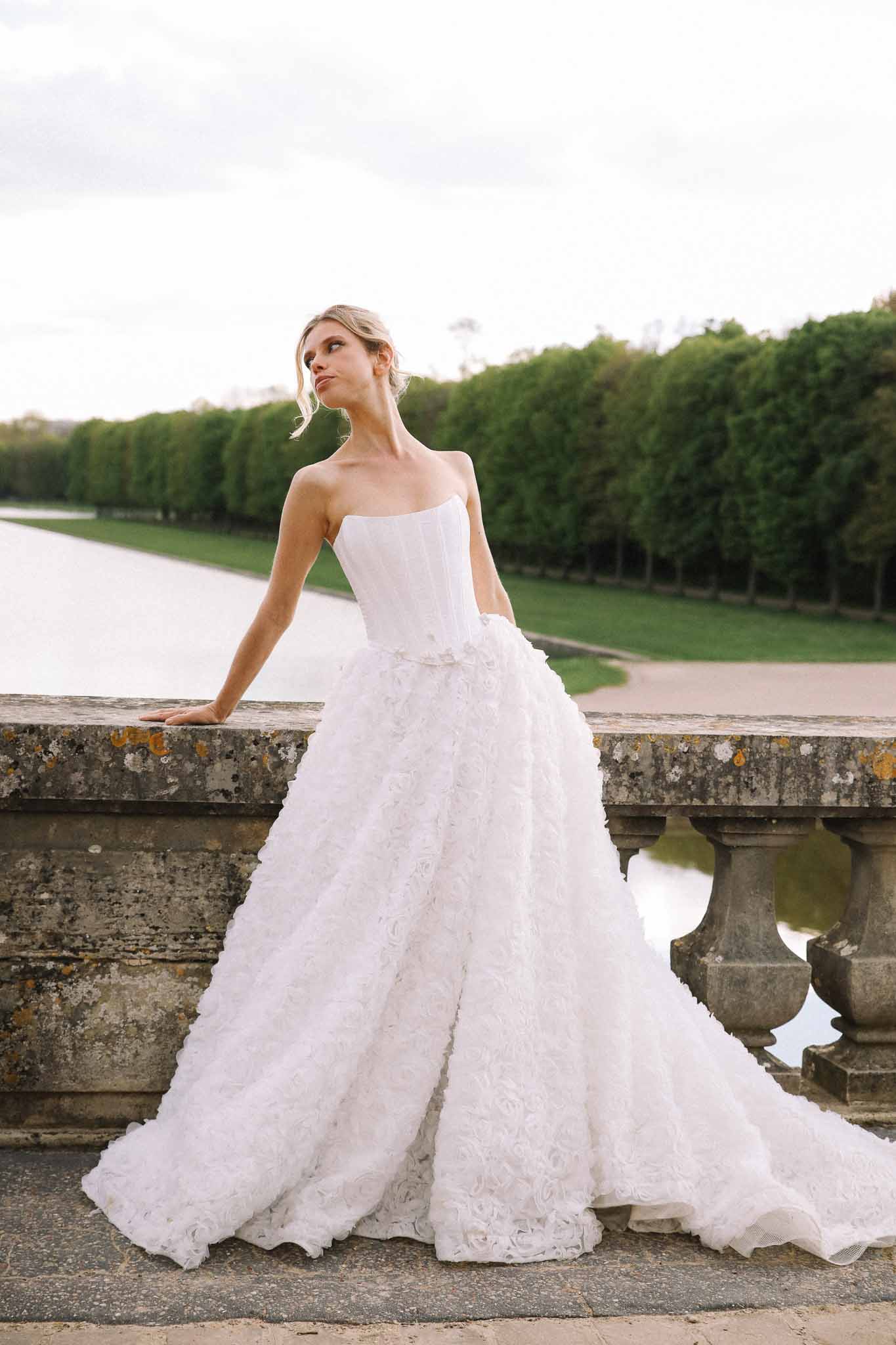 Bride in white wedding gown posing on stone bridge in formal garden with hedges and water canal