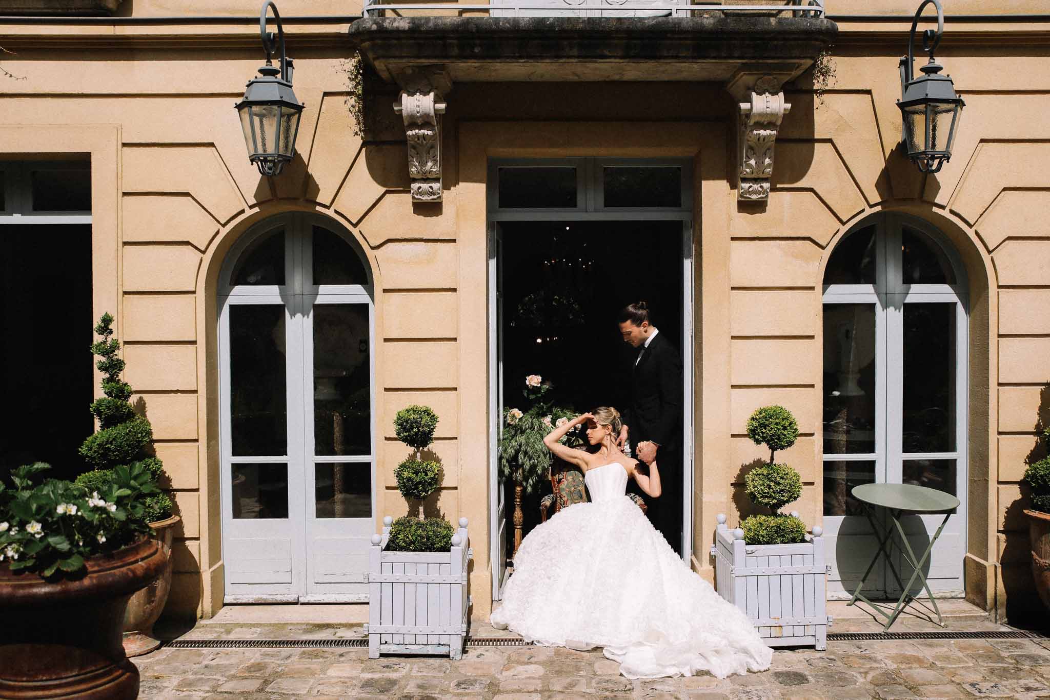 Bride and groom entering classical stone courtyard with arched windows and formal gardens