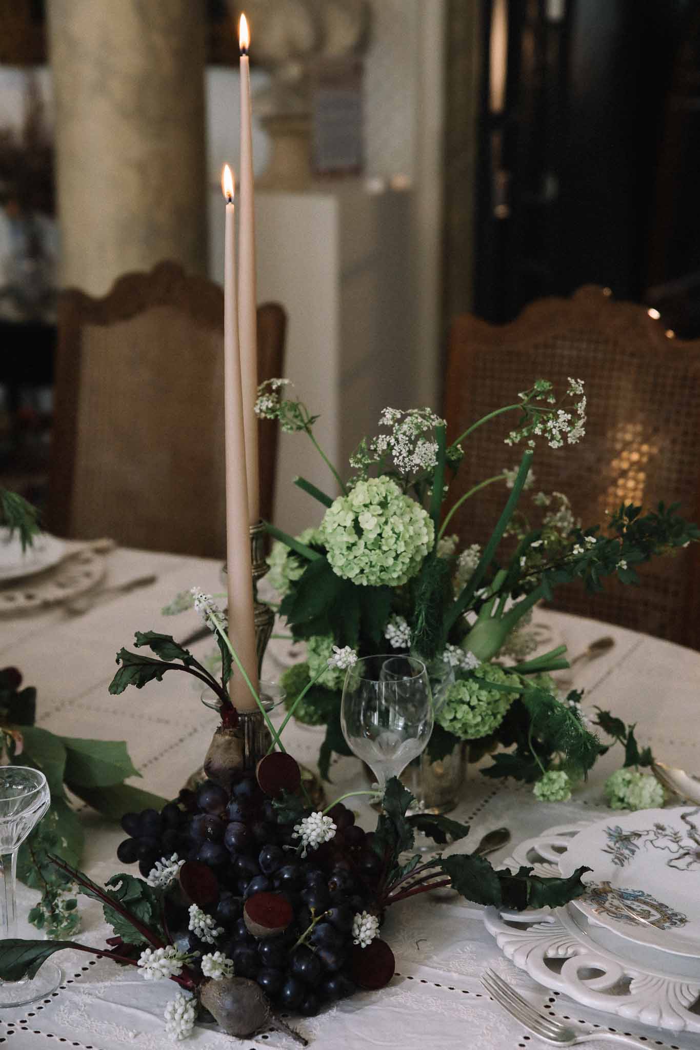 Reception table centerpiece with candles, fruit, and greenery at elegant indoor wedding venue
