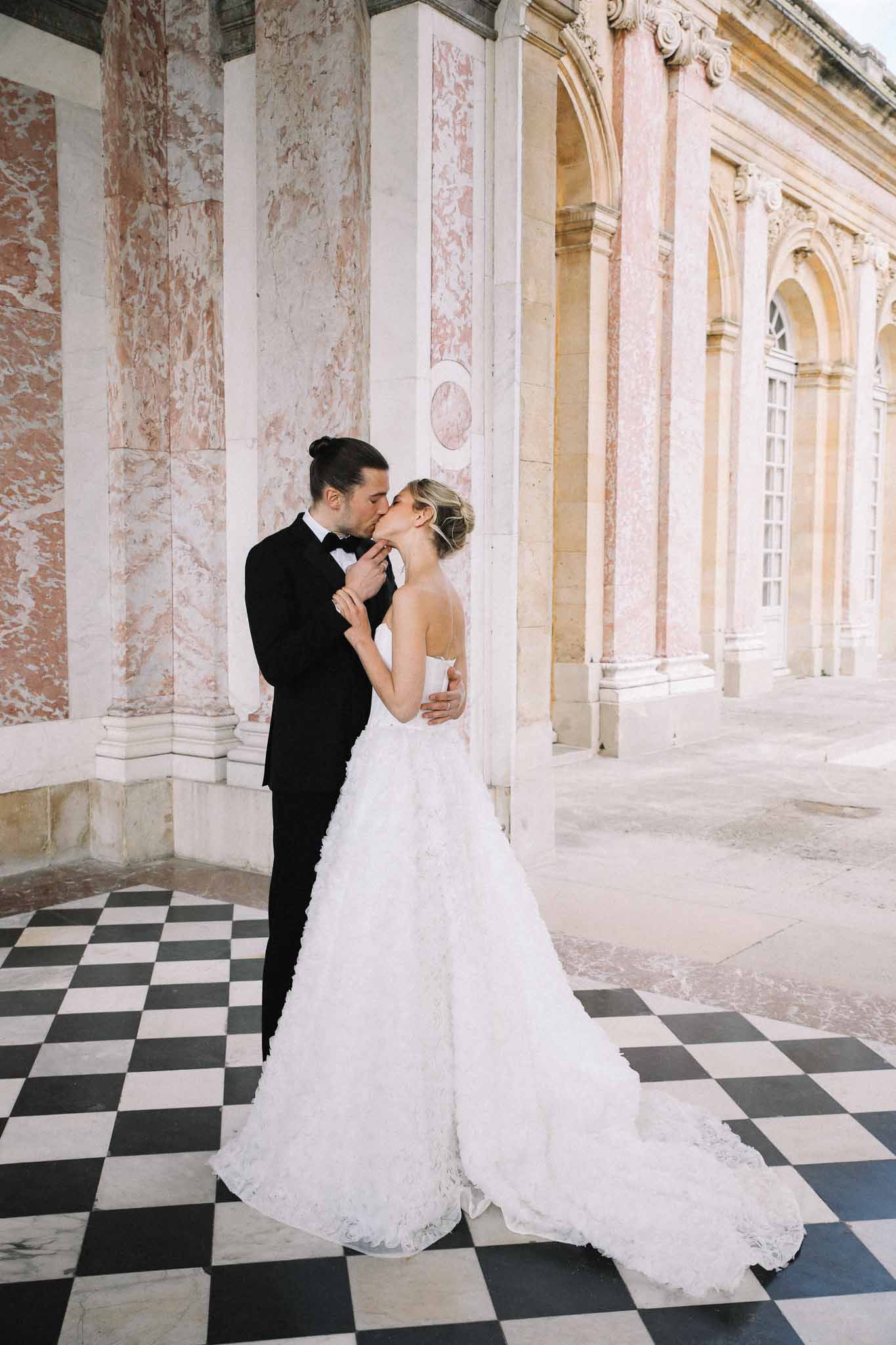 Bride and groom kissing in neoclassical columned corridor with marble floors